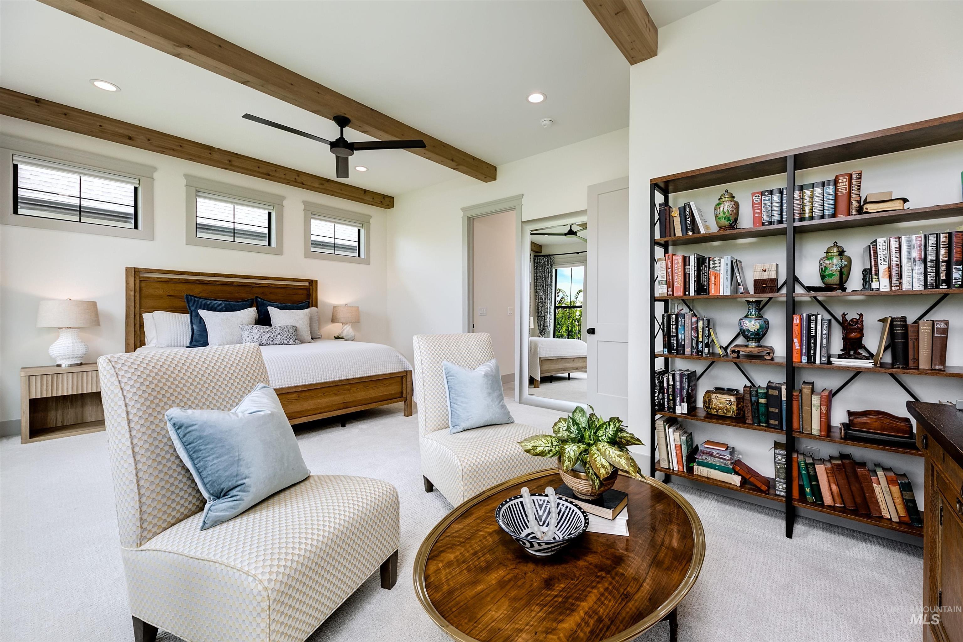Spacious bedroom featuring decorative wood ceiling beams, white wall finishes, light-toned carpet flooring, a ceiling fan, and a built-in shelving unit