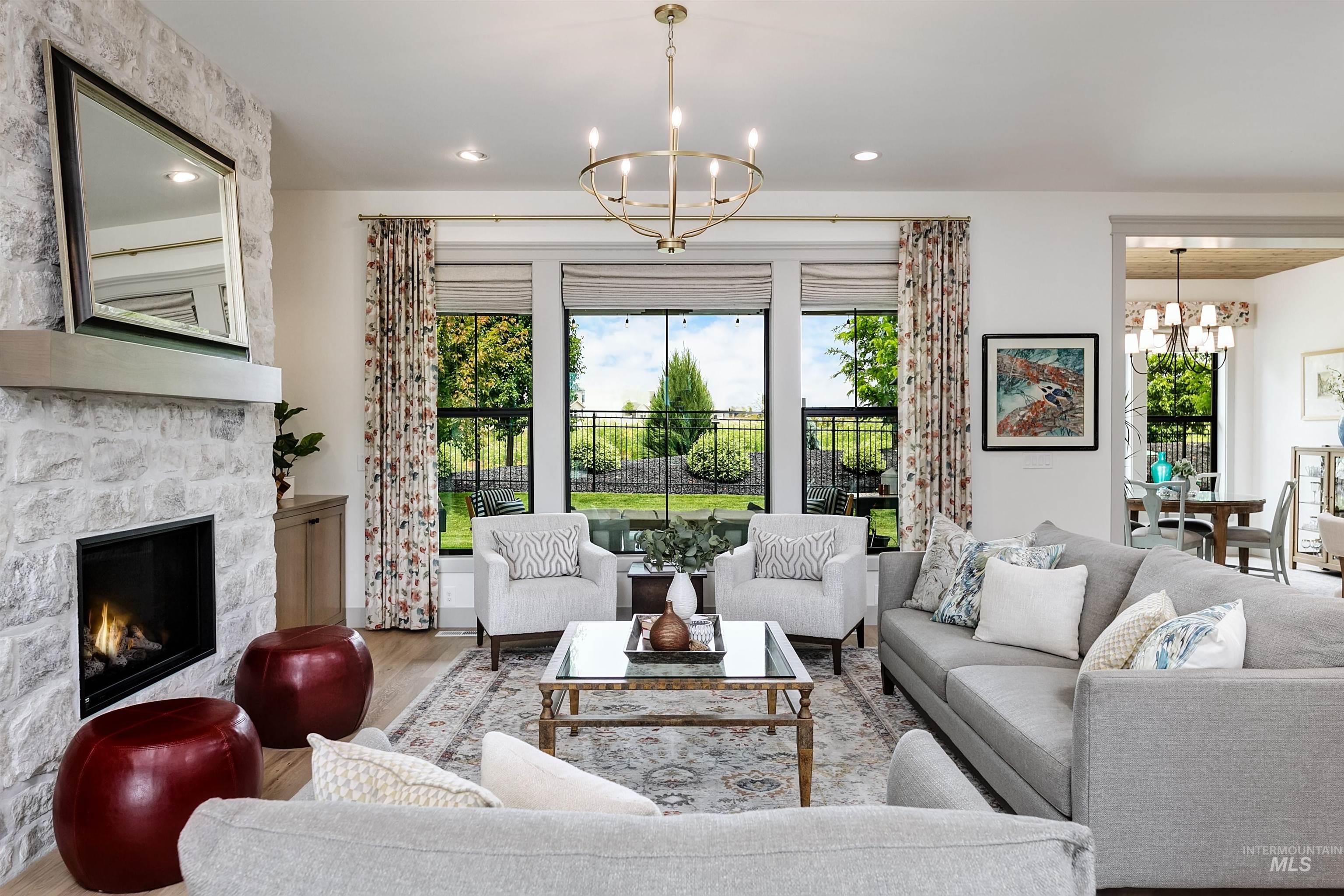Spacious living area featuring a stone fireplace with hearth, a prominent chandelier, wood-finish flooring, and expansive windows