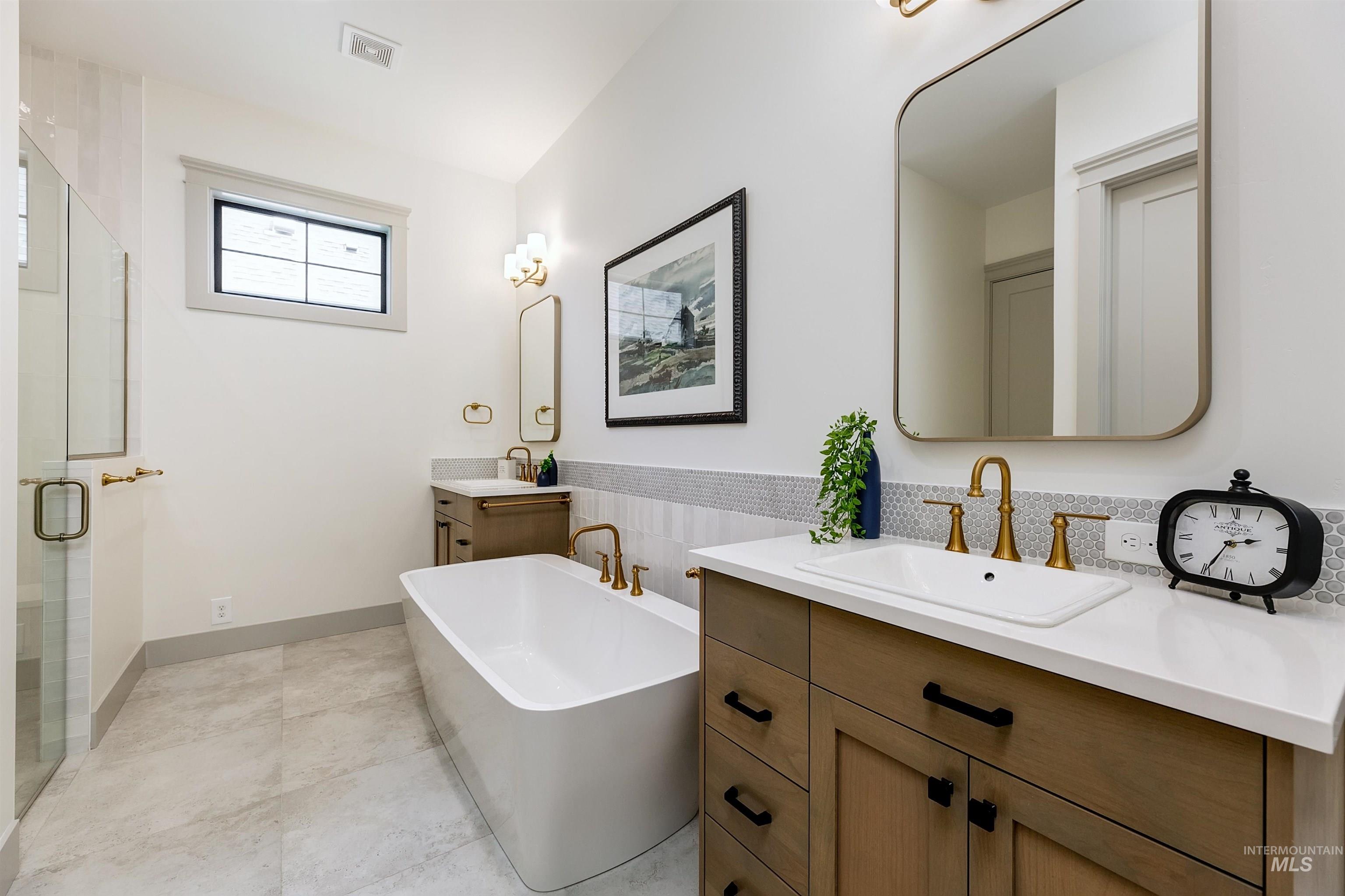 Bathroom featuring a freestanding soaking tub, dual vanity with wood-finish cabinetry, frameless glass shower enclosure, and light-toned floor tiling