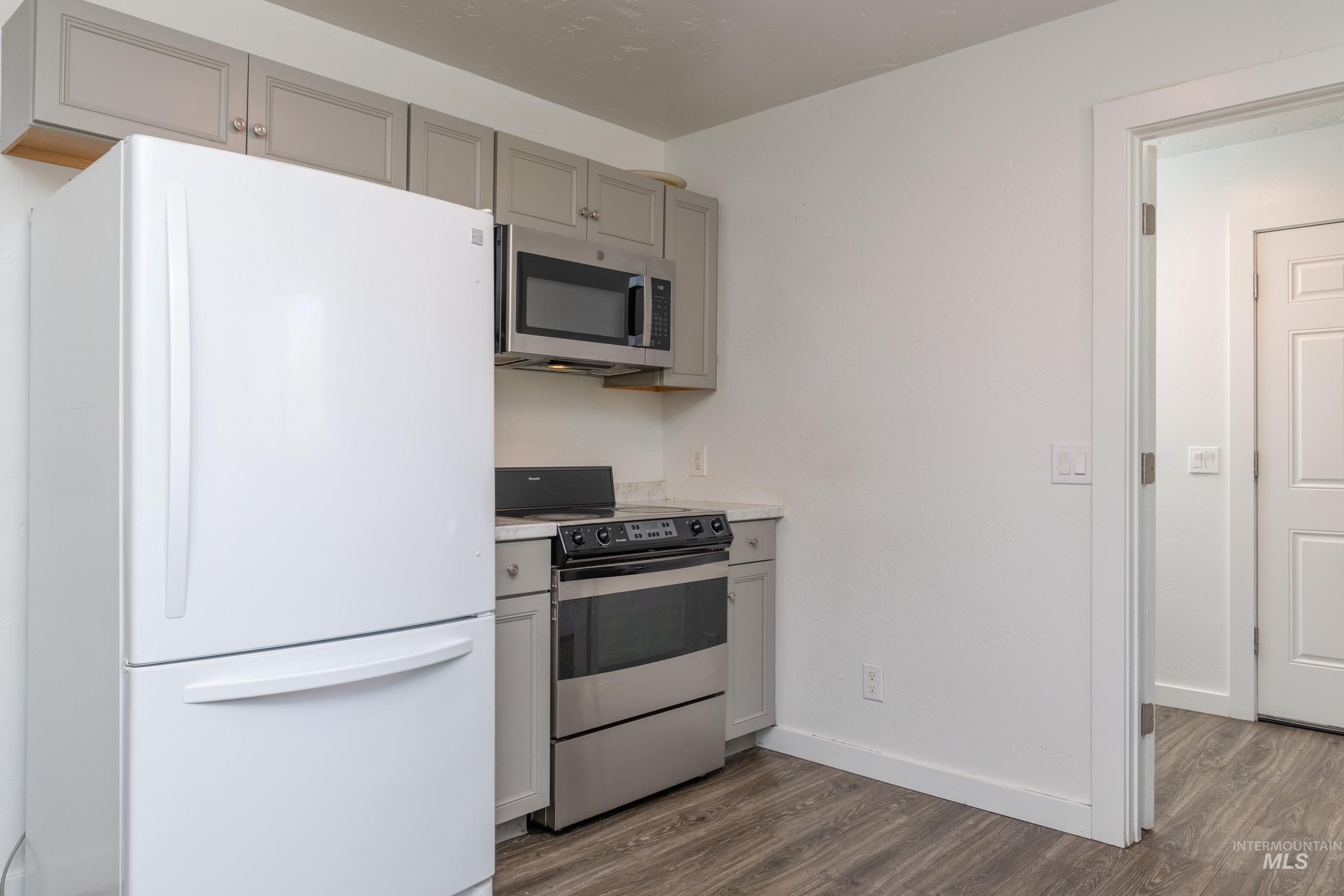 Kitchen with gray cabinetry, appliances with stainless steel finishes, light countertops, and dark wood-style flooring
