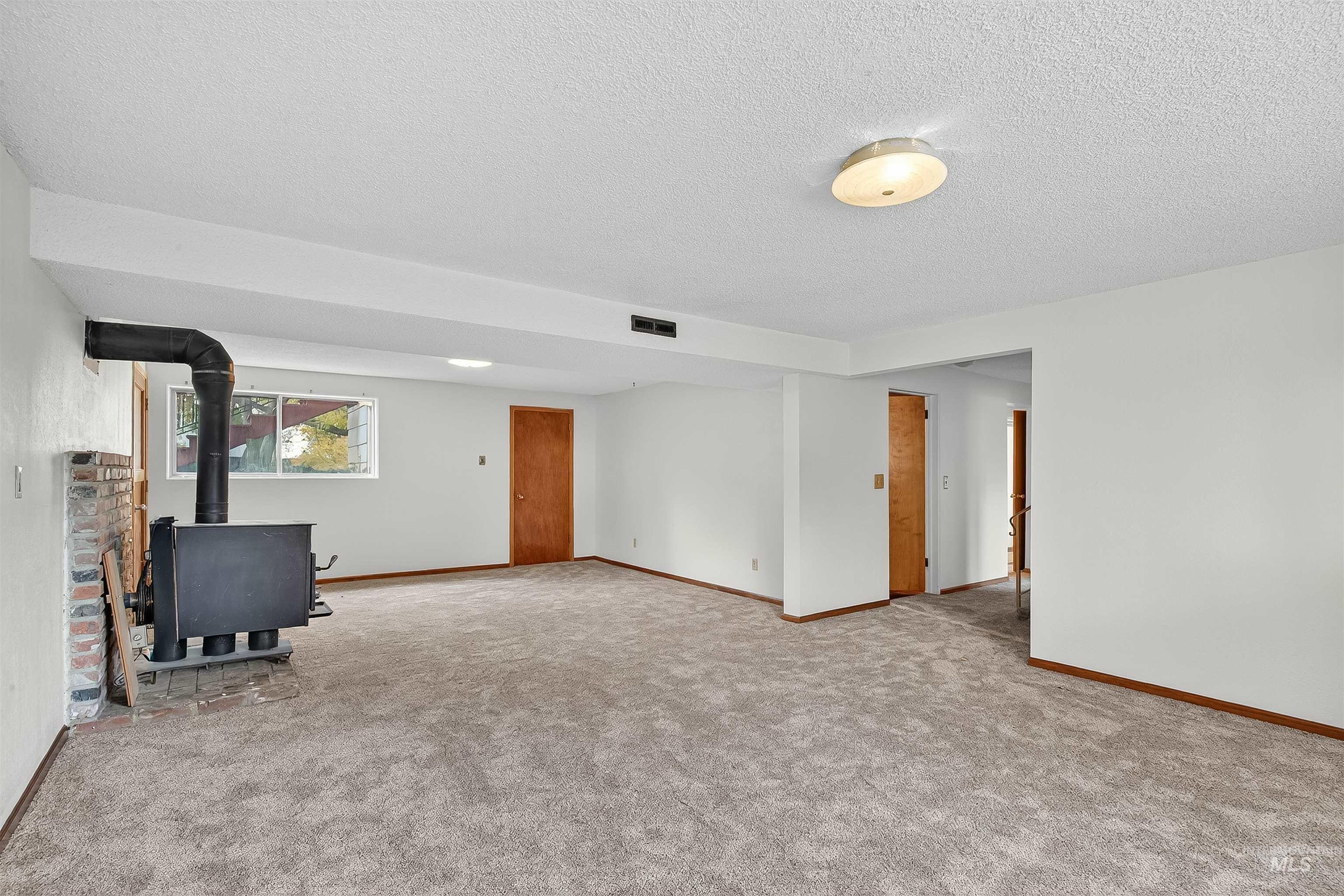 Unfurnished living room with a wood stove, a textured ceiling, and light colored carpet