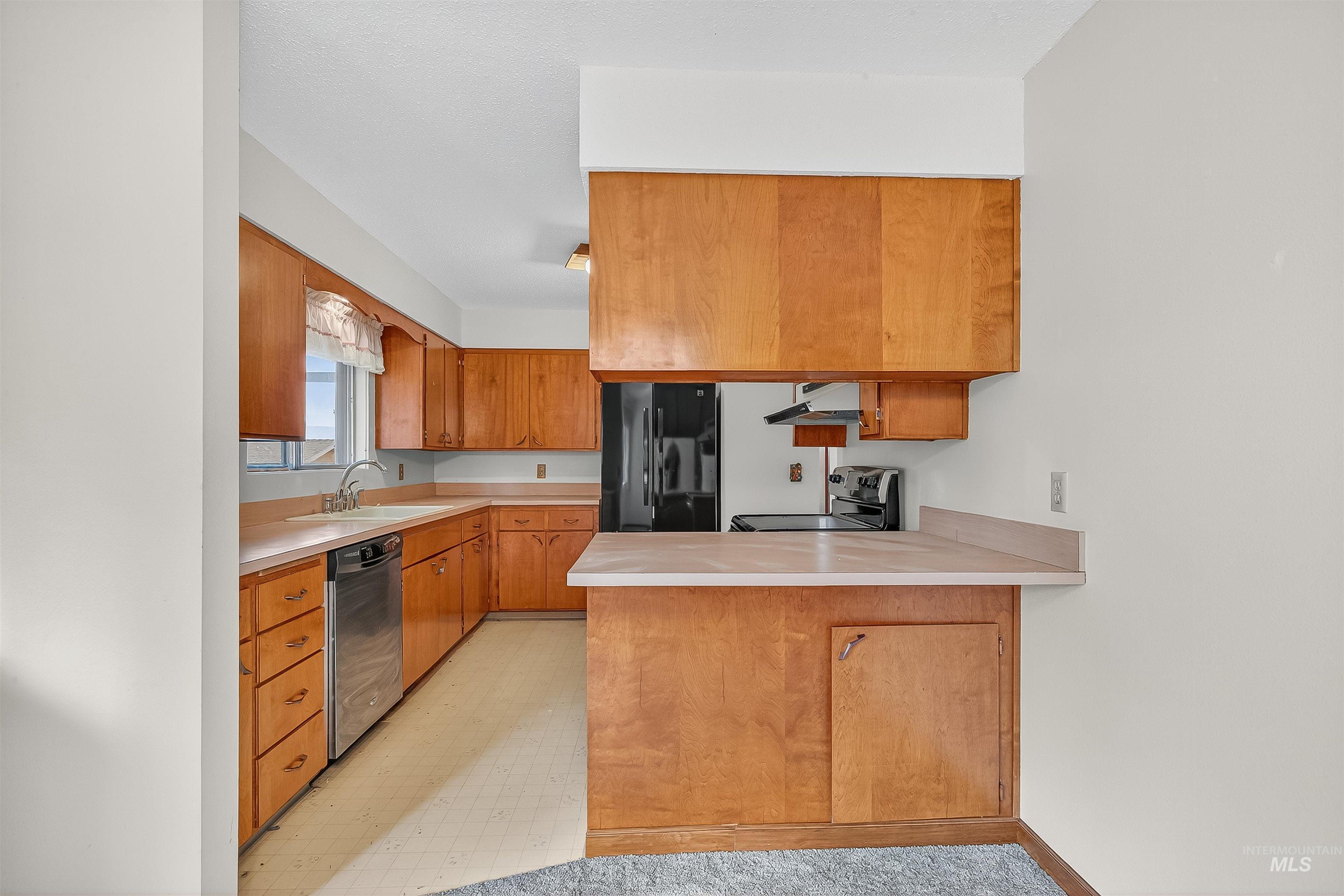 Kitchen featuring light countertops, brown cabinets, a peninsula, stainless steel appliances, and under cabinet range hood