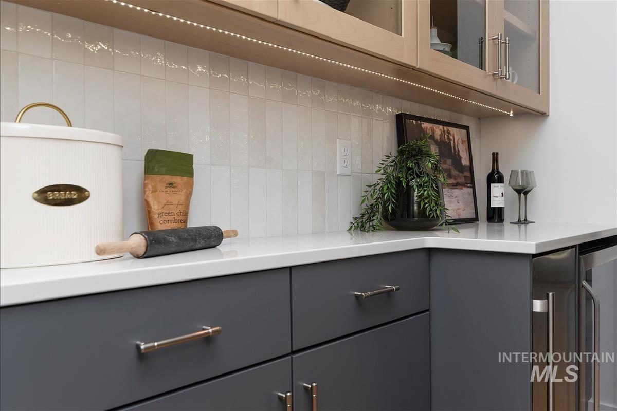 Detailed view of gray cabinets, beverage cooler, light countertops, glass insert cabinets, and decorative backsplash