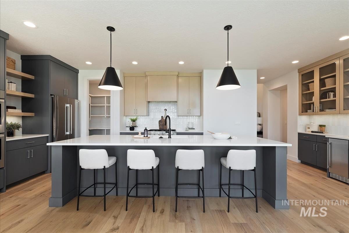 Kitchen with open shelves, light wood finished floors, a kitchen island with sink, light countertops, and recessed lighting