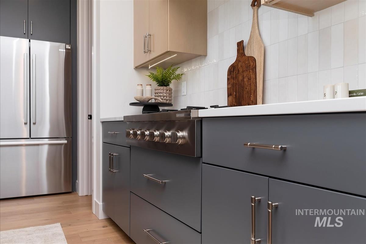 Kitchen featuring freestanding refrigerator, light wood-style floors, tasteful backsplash, gray cabinetry, and light countertops