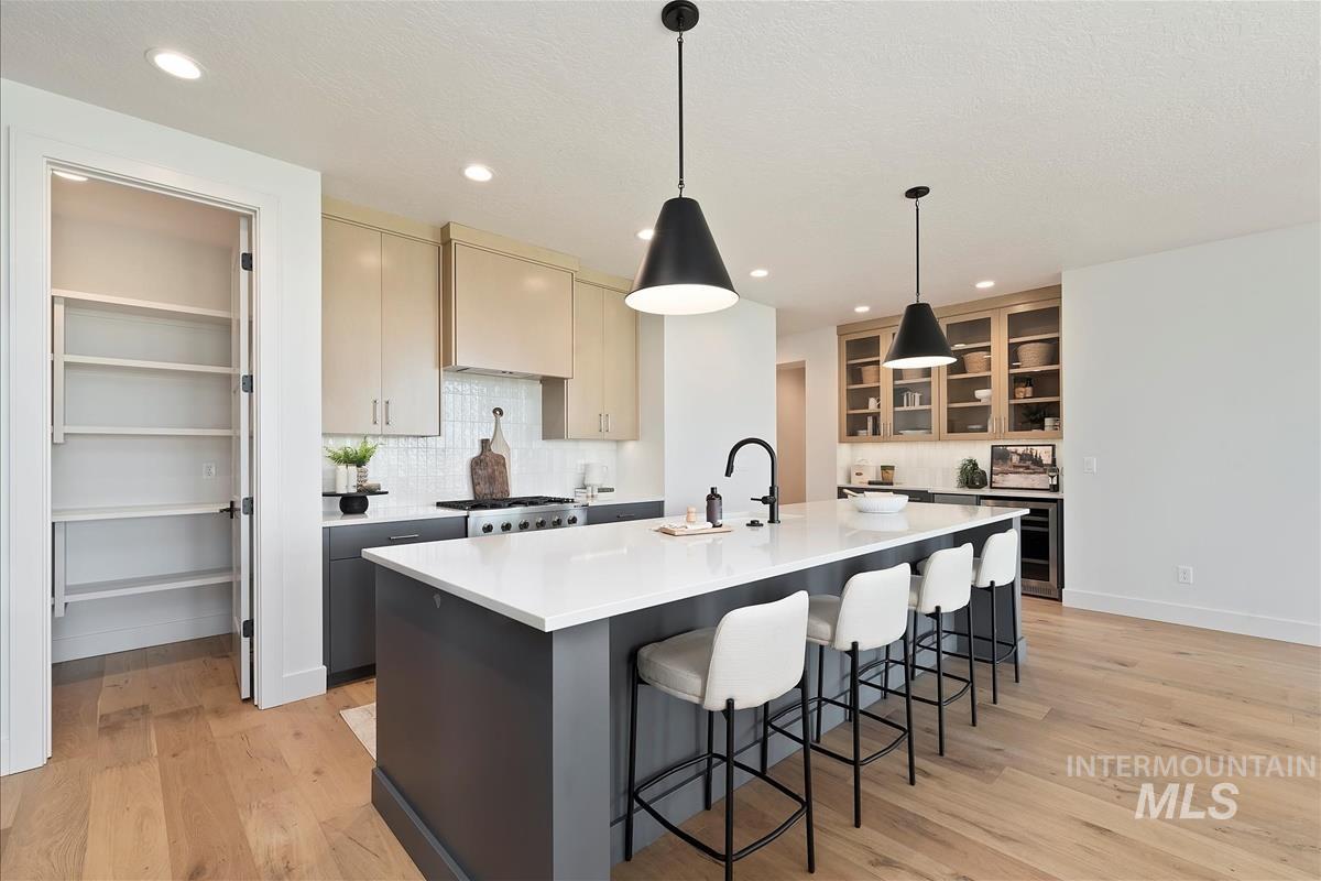 Kitchen featuring tasteful backsplash, light wood-style floors, a center island with sink, light countertops, and recessed lighting
