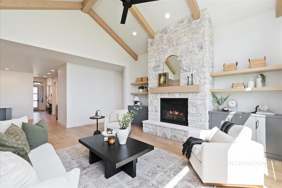 Living area featuring a ceiling fan, a stone fireplace, light wood-type flooring, beamed ceiling, and high vaulted ceiling