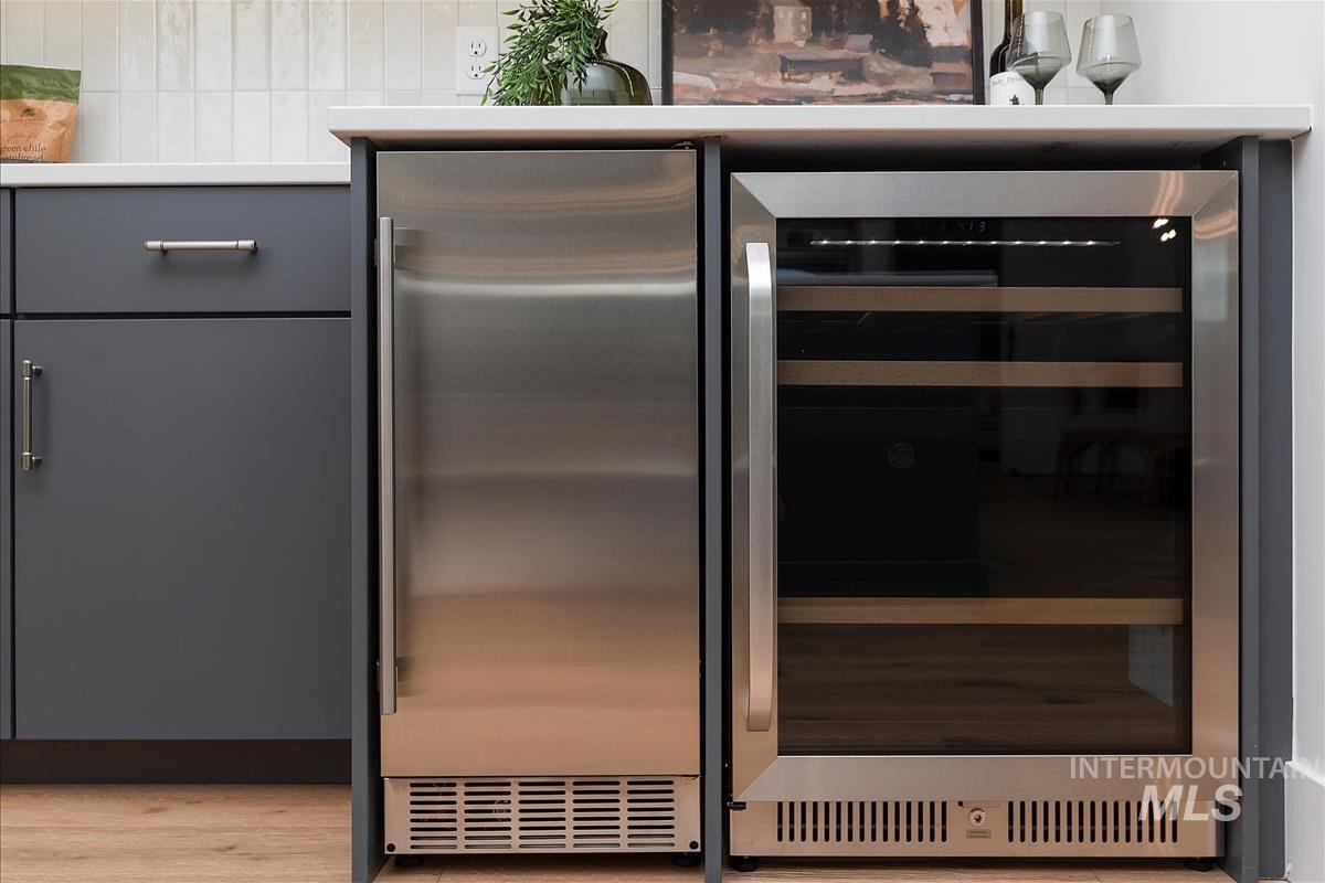 Kitchen view of beverage cooler, gray cabinetry, wood finished floors, and backsplash