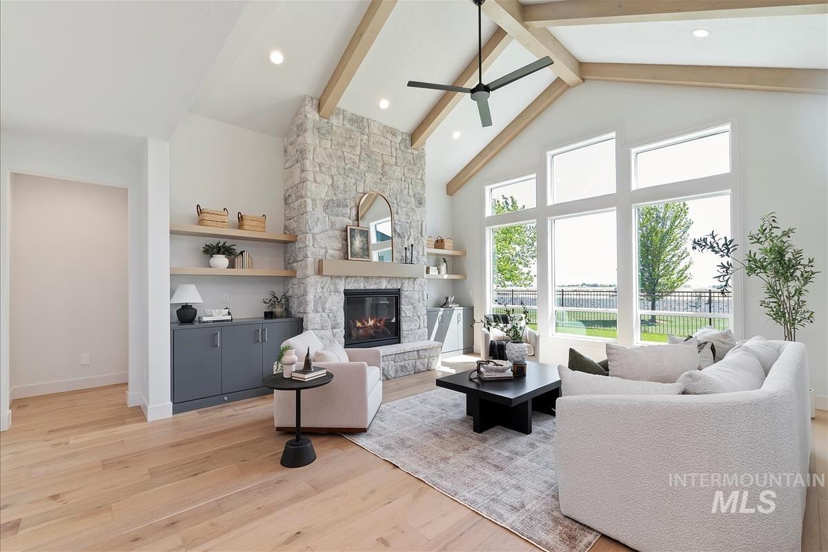 Living area featuring ceiling fan, a fireplace, beamed ceiling, high vaulted ceiling, and light wood-style flooring