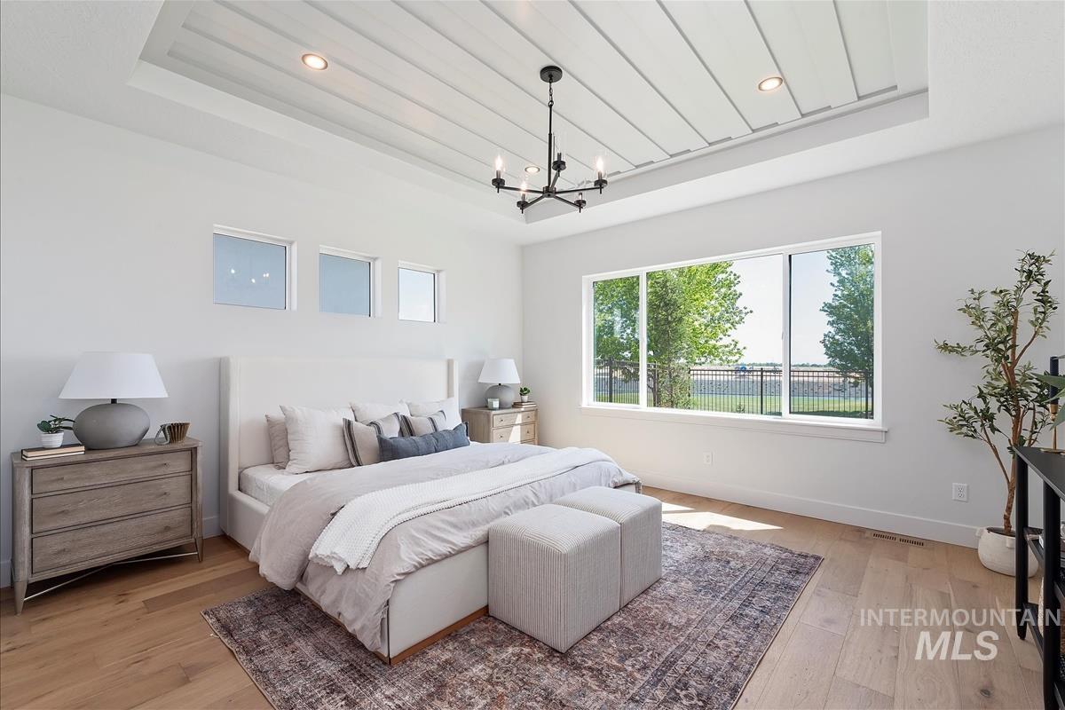 Bedroom featuring a tray ceiling, a chandelier, light wood-style floors, and recessed lighting