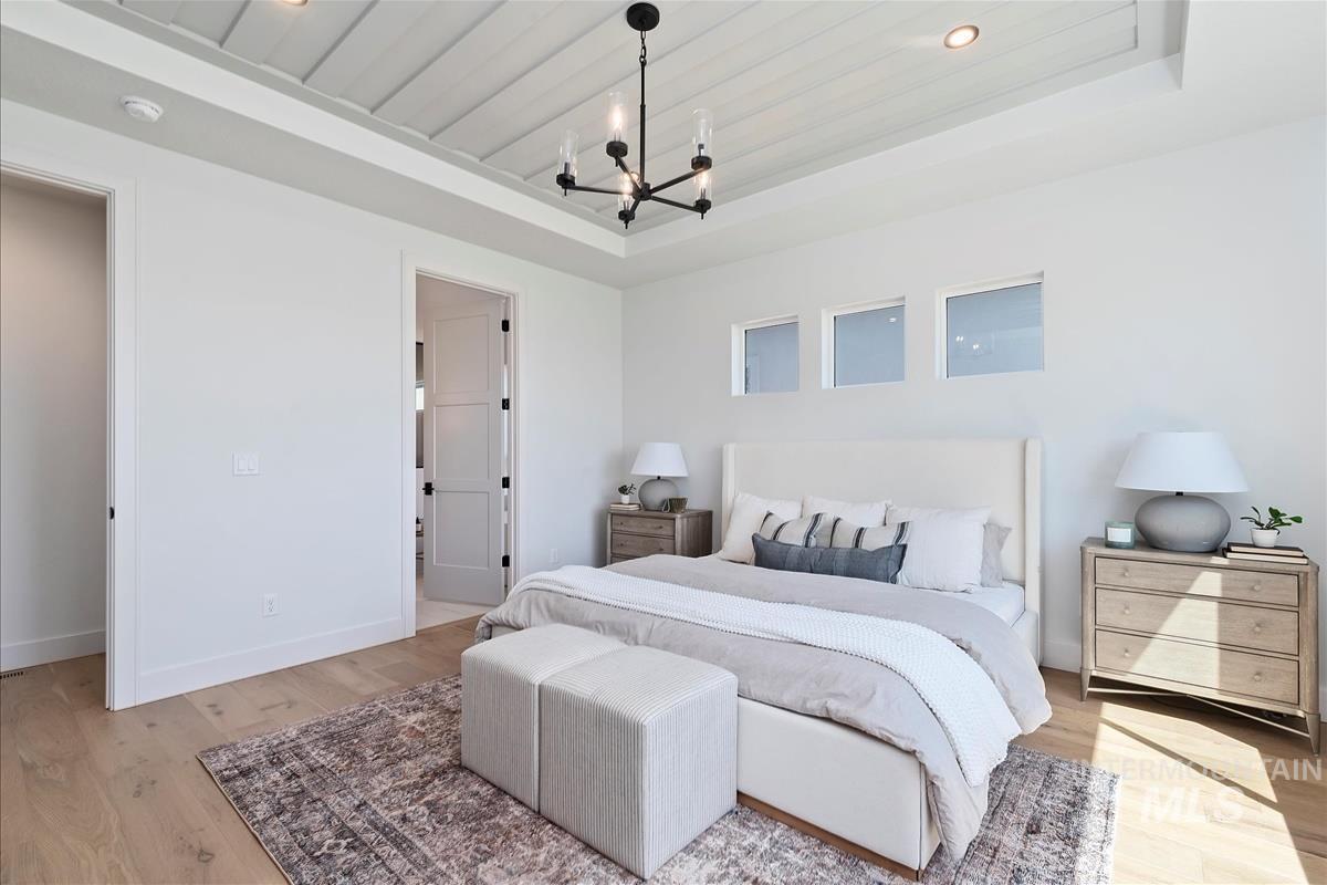 Bedroom with a raised ceiling, a chandelier, light wood-style floors, and recessed lighting
