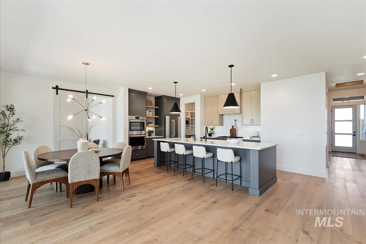 Kitchen featuring open shelves, light countertops, light wood-style flooring, a kitchen island with sink, and a kitchen breakfast bar