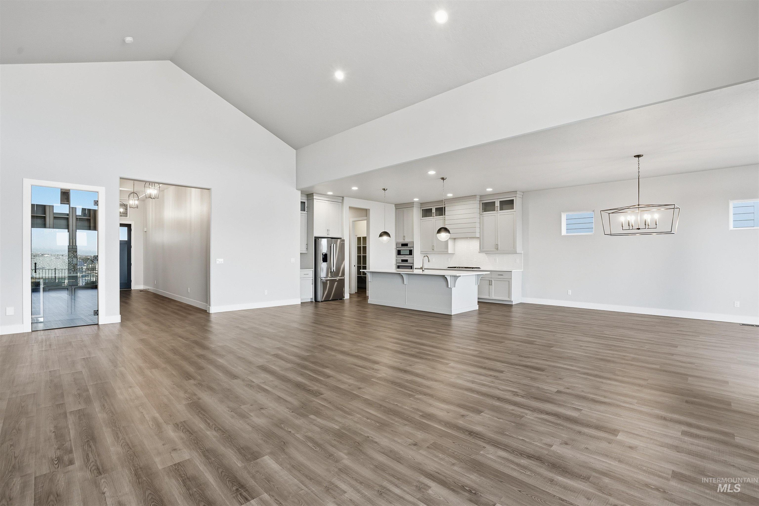 Unfurnished living room with a chandelier, dark wood-style flooring, high vaulted ceiling, and recessed lighting