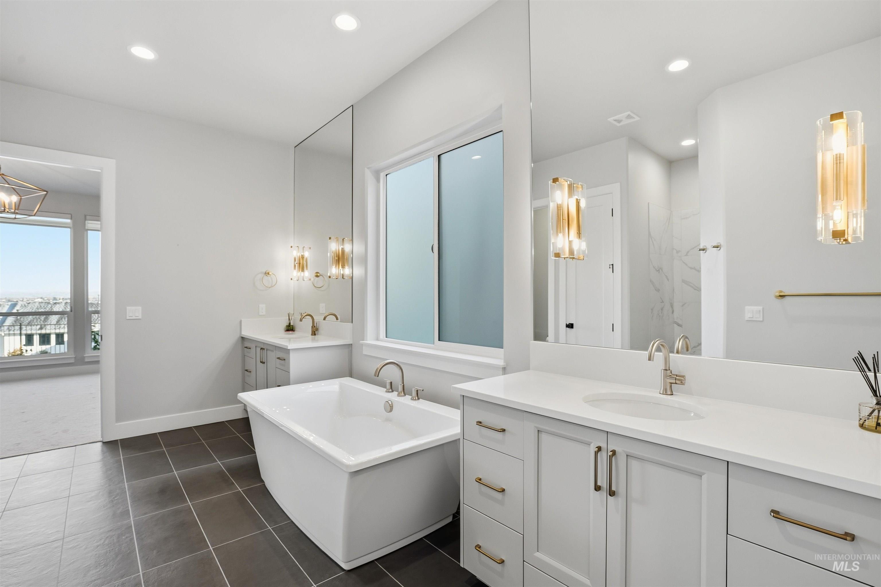 Full bath featuring a freestanding bath, two vanities, recessed lighting, and dark tile patterned flooring