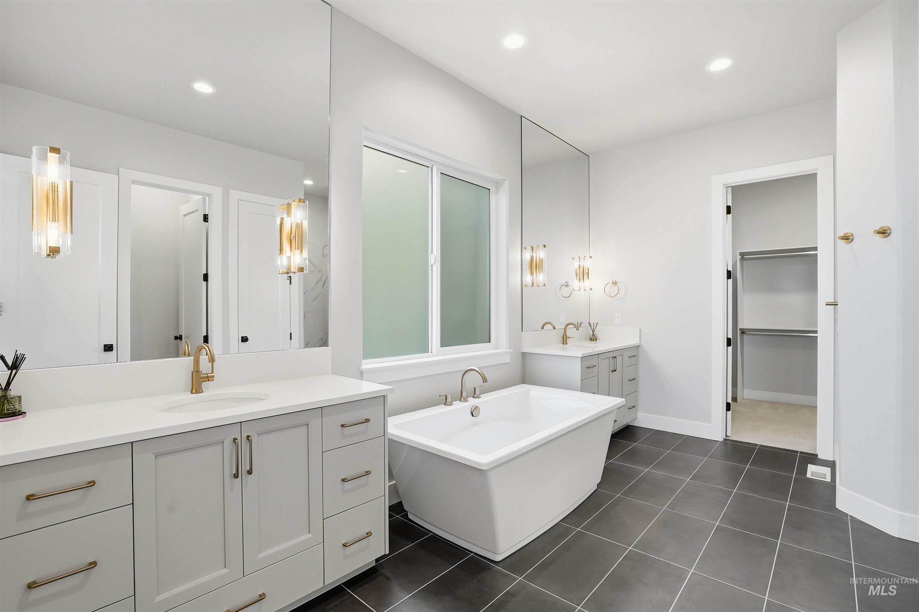 Full bathroom with two vanities, a soaking tub, recessed lighting, dark tile patterned flooring, and a spacious closet