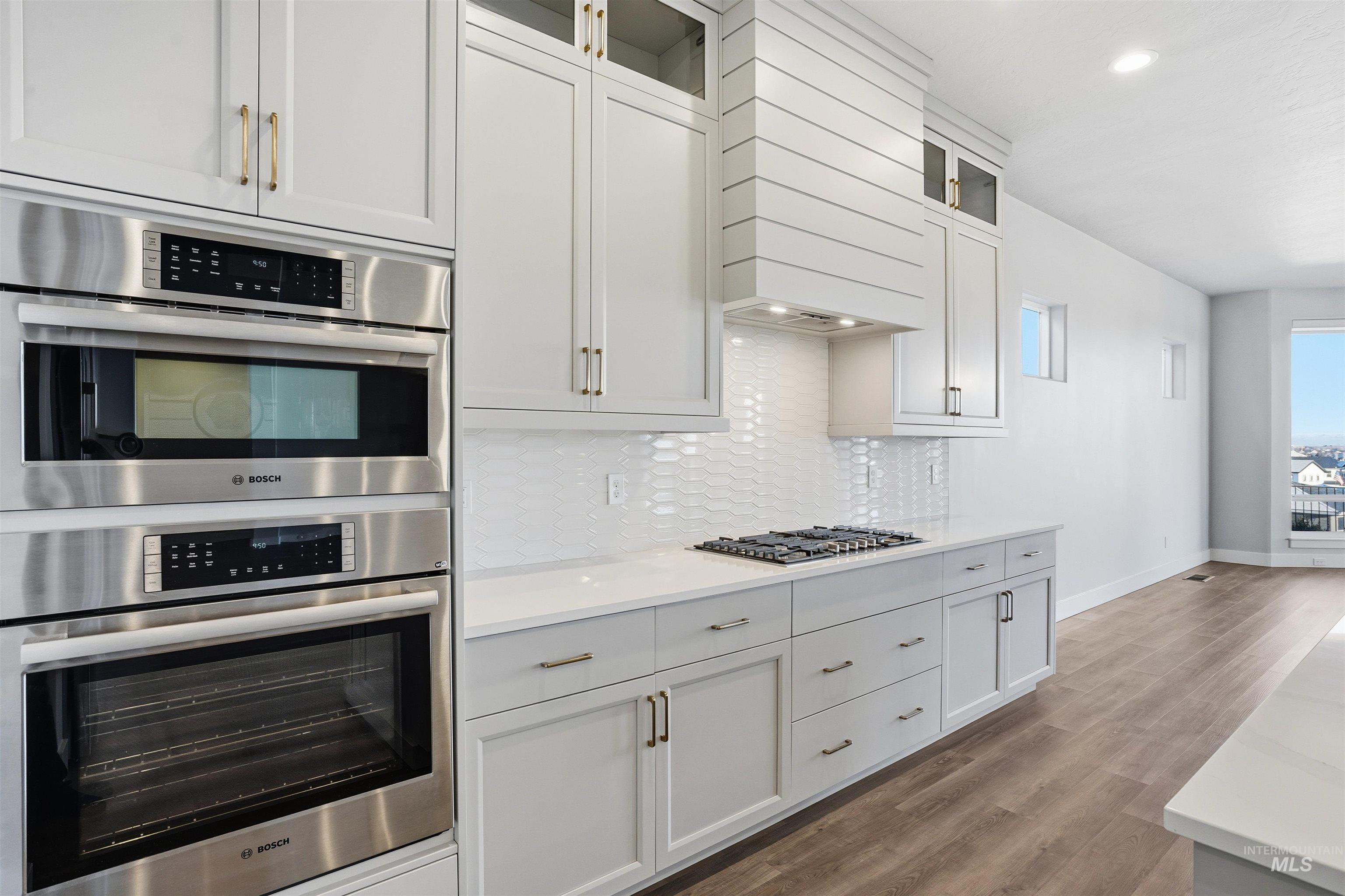 Kitchen featuring stainless steel appliances, glass insert cabinets, dark wood-type flooring, light stone countertops, and white cabinetry