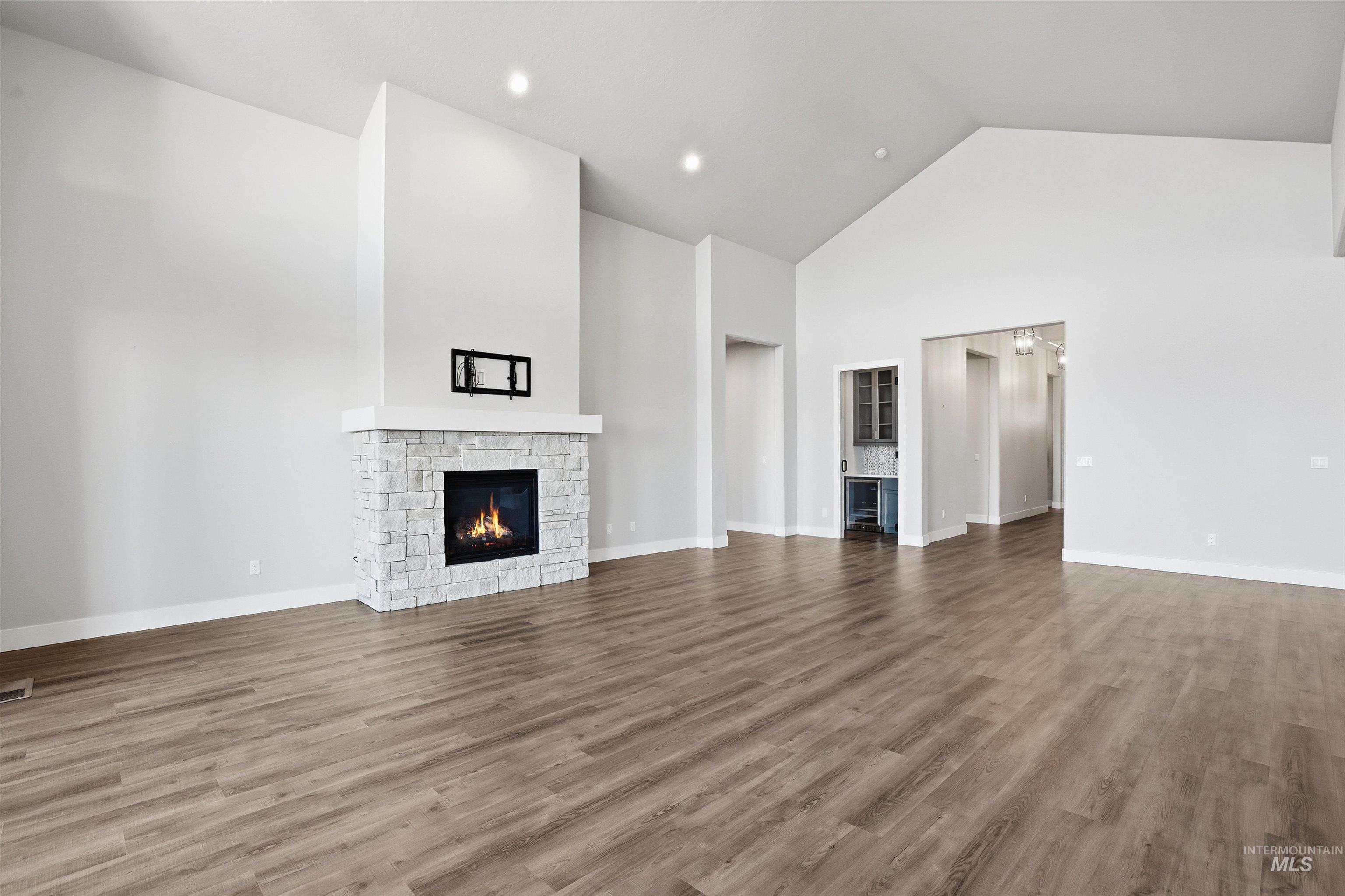Unfurnished living room featuring a stone fireplace, high vaulted ceiling, wood finished floors, and recessed lighting