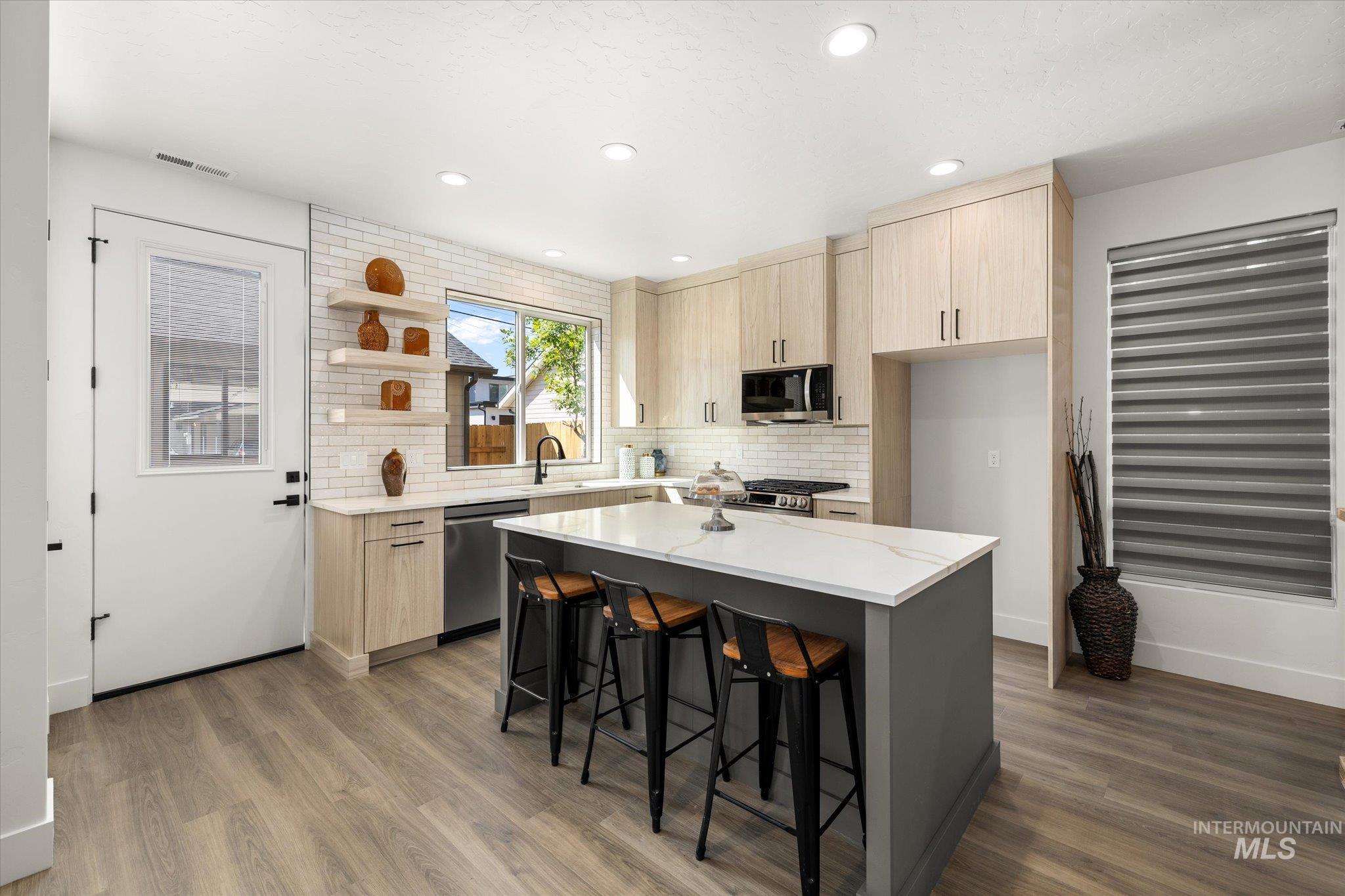 Kitchen with light brown cabinets, light stone counters, decorative backsplash, modern cabinets, and recessed lighting