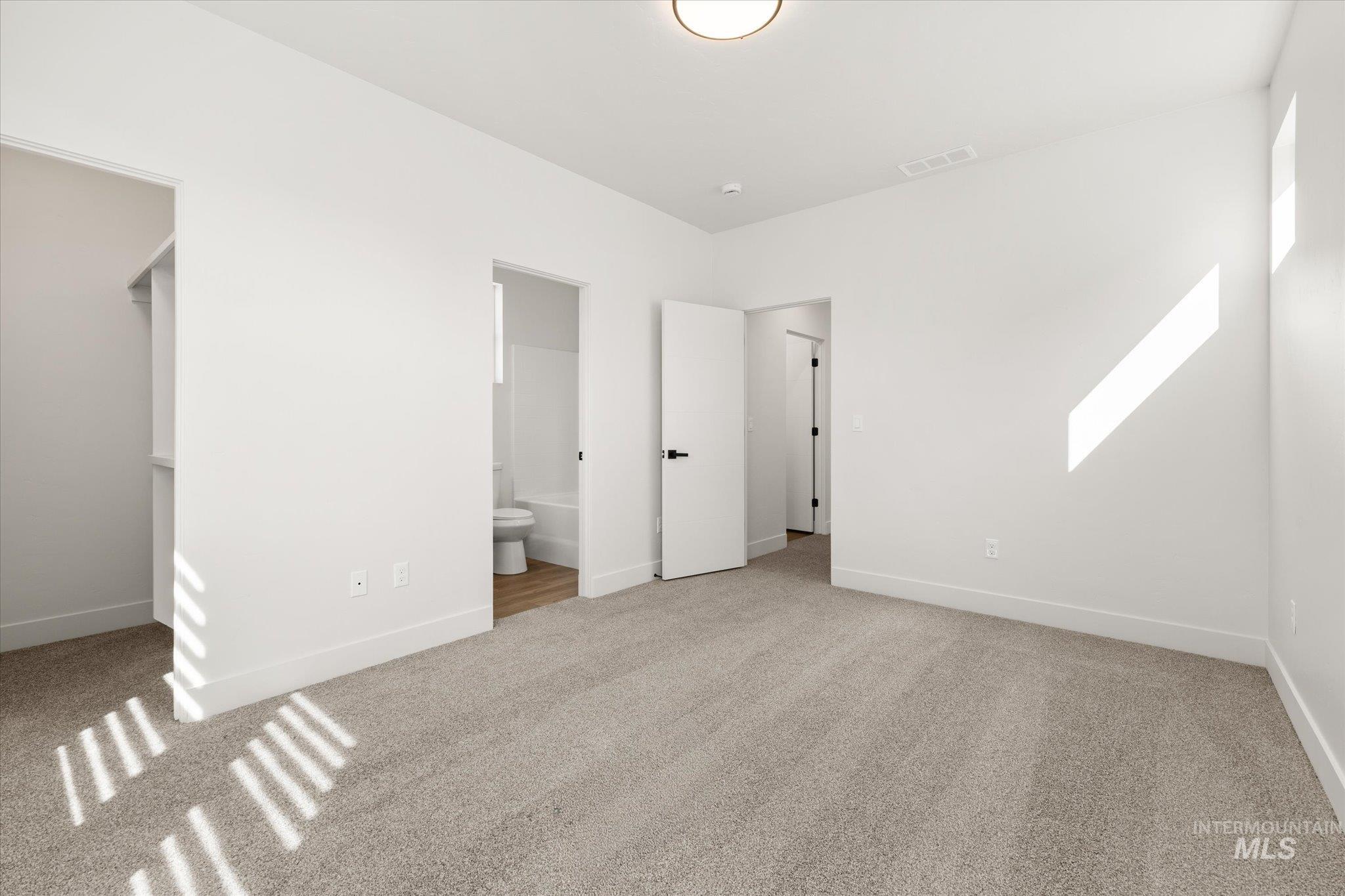 Unfurnished bedroom featuring light carpet, a walk in closet, and ensuite bathroom
