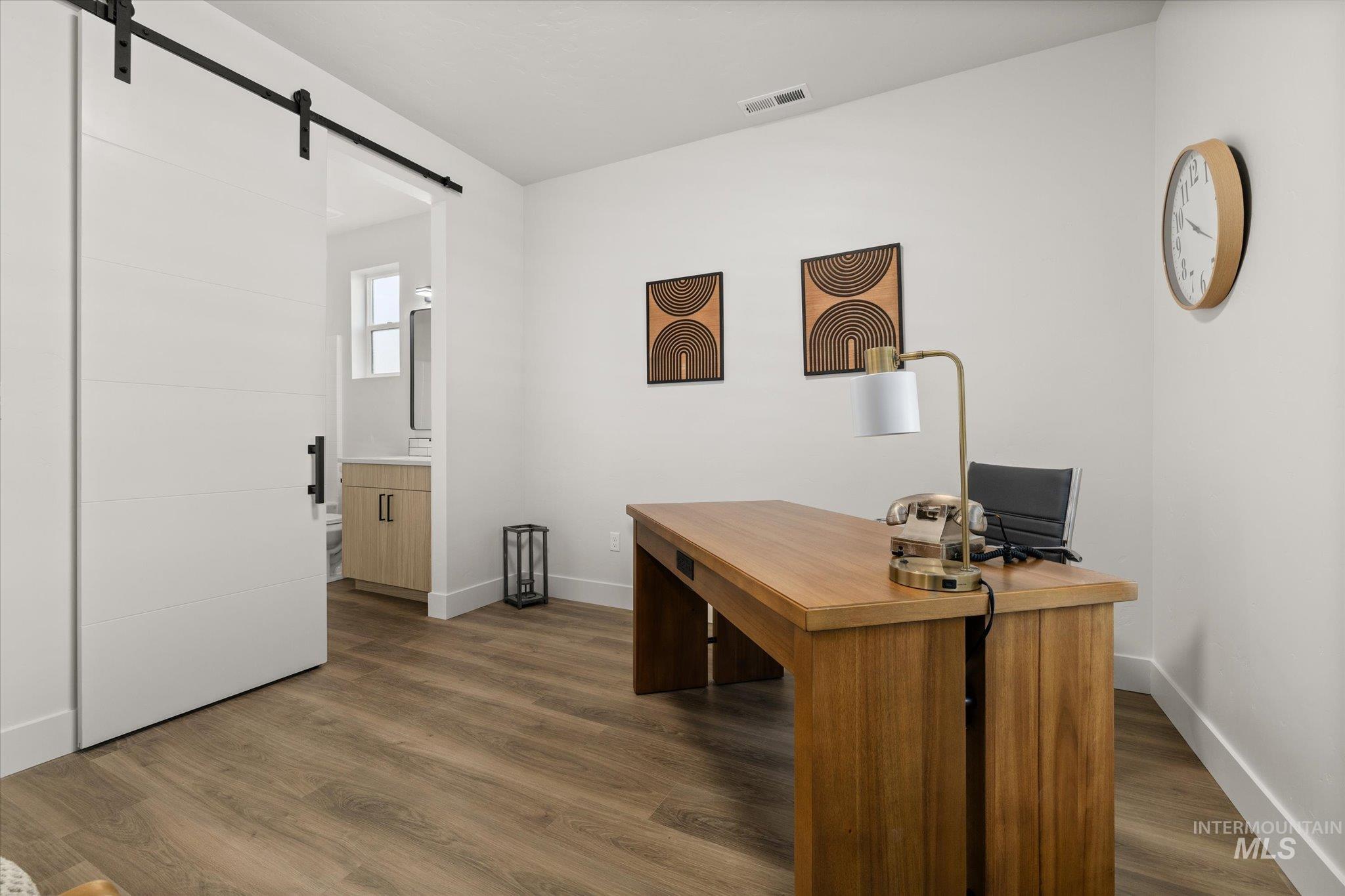 Office with a barn door and dark wood-type flooring