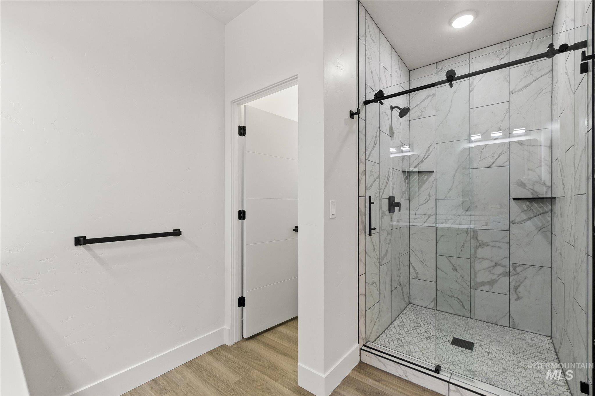 Full bath with a marble finish shower and light wood-type flooring