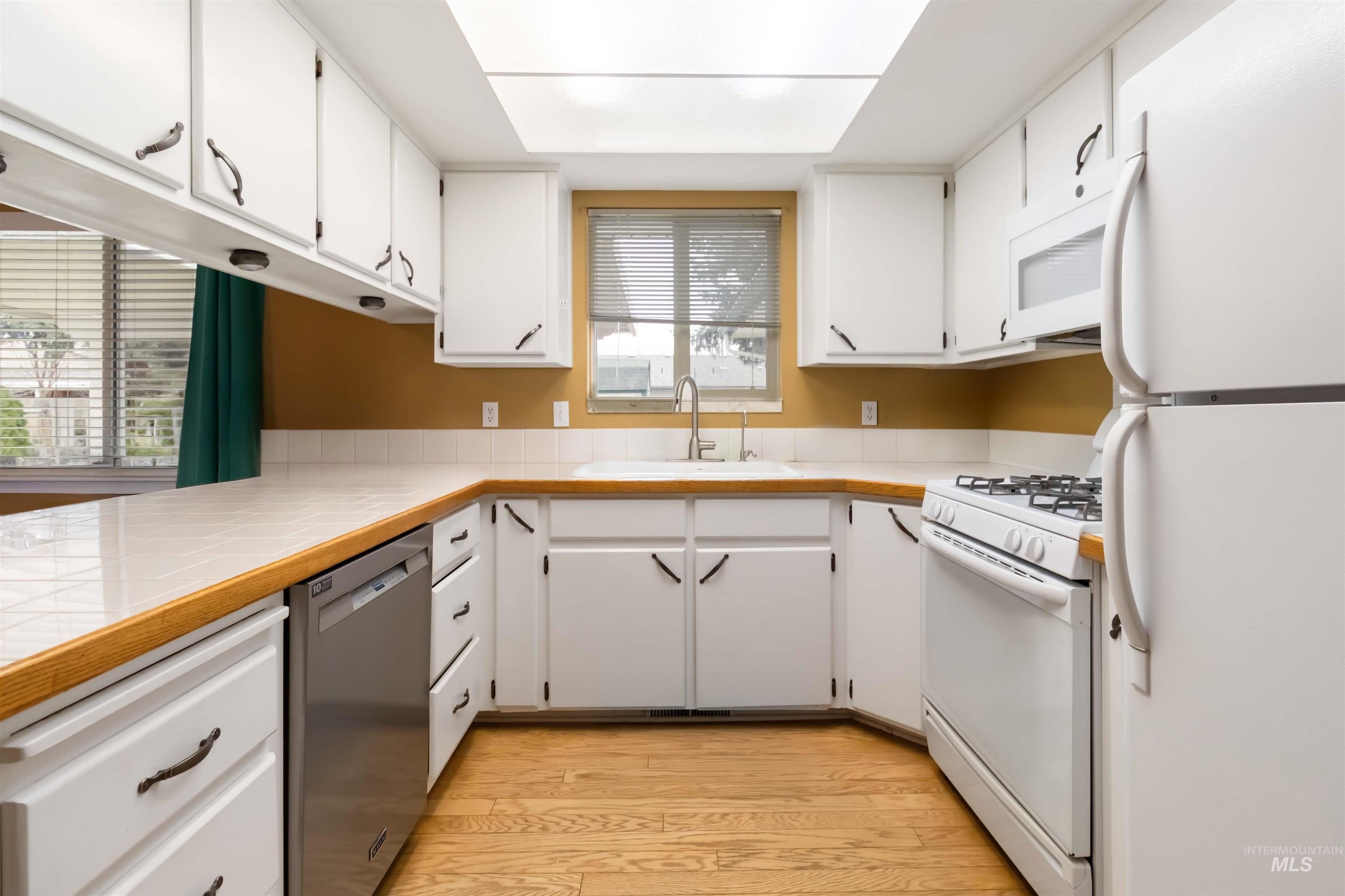 Kitchen with white appliances, white cabinets, tile countertops, and light wood-type flooring