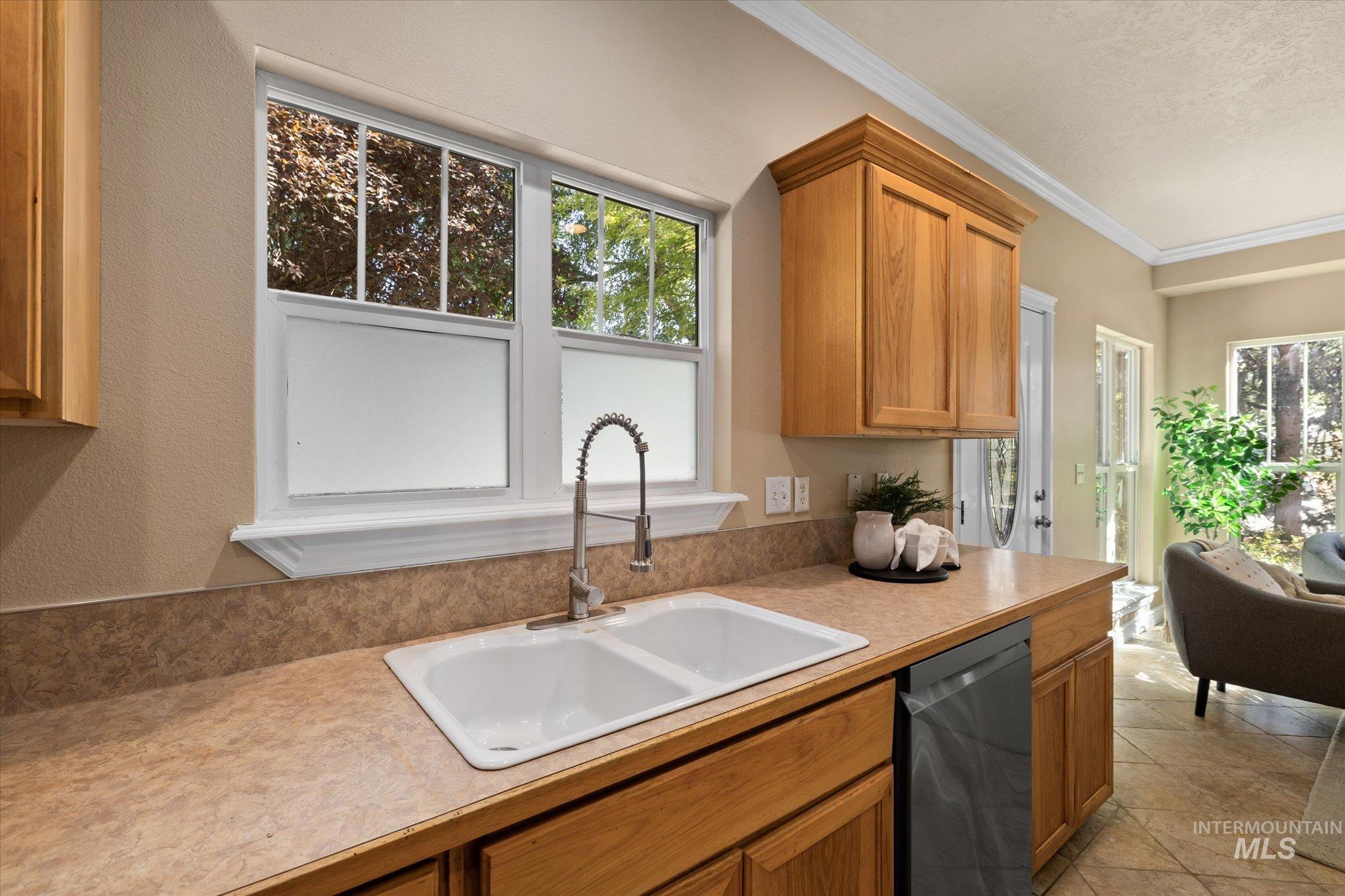 Kitchen with stainless steel dishwasher, healthy amount of natural light, light countertops, ornamental molding, and brown cabinets