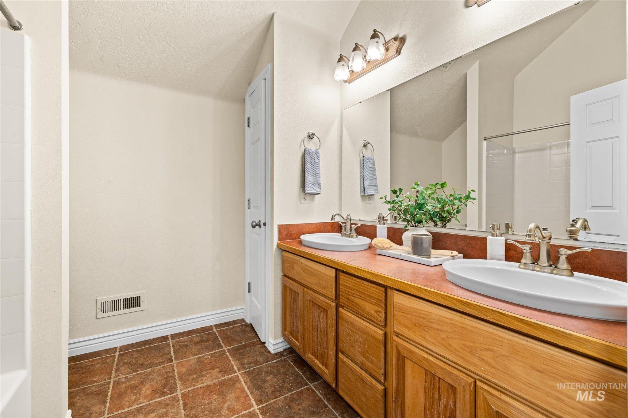 Full bathroom featuring double vanity, dark tile patterned floors,  shower combination, and a textured ceiling