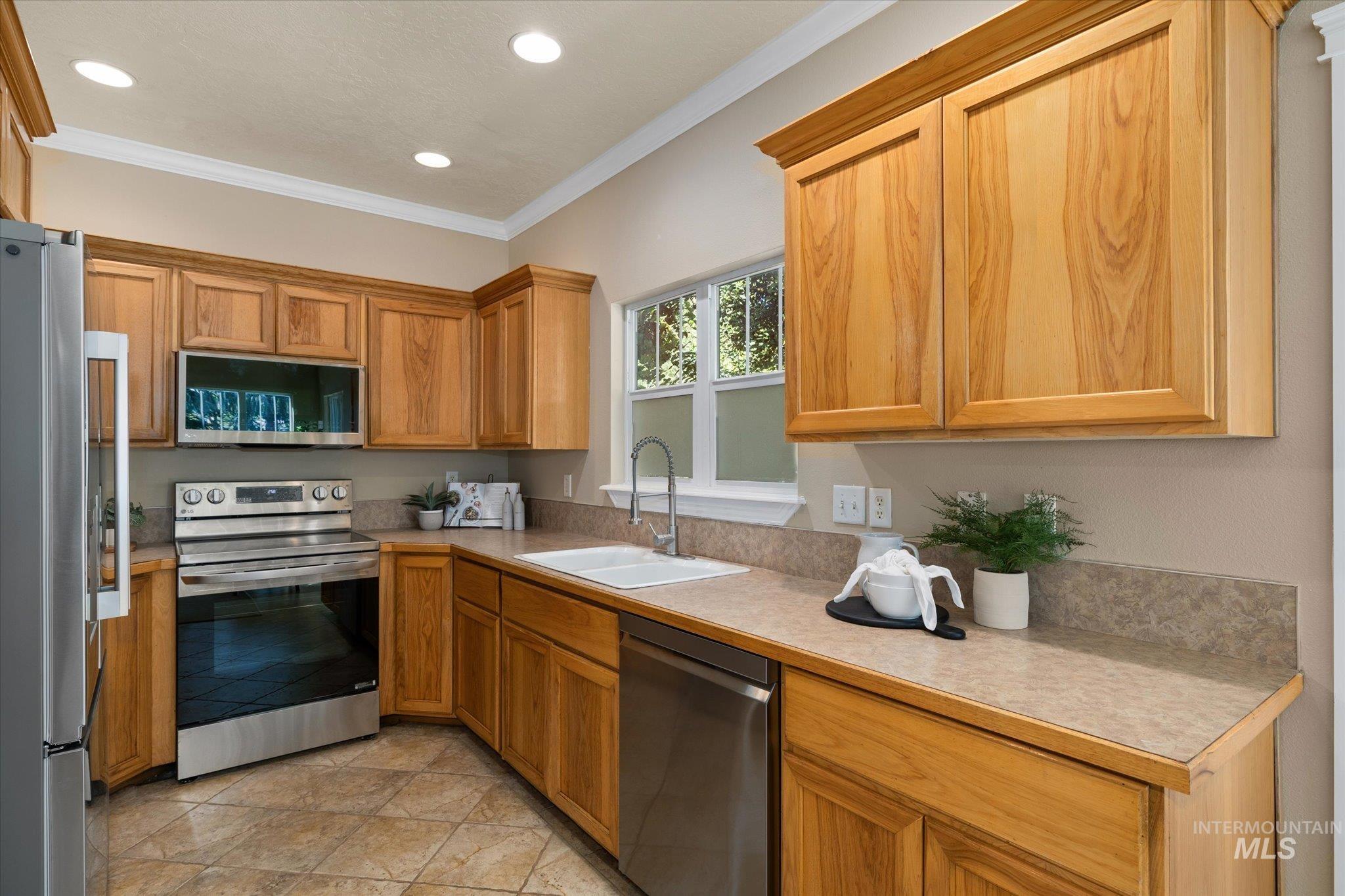 Kitchen with stainless steel appliances, light countertops, crown molding, recessed lighting, and brown cabinets