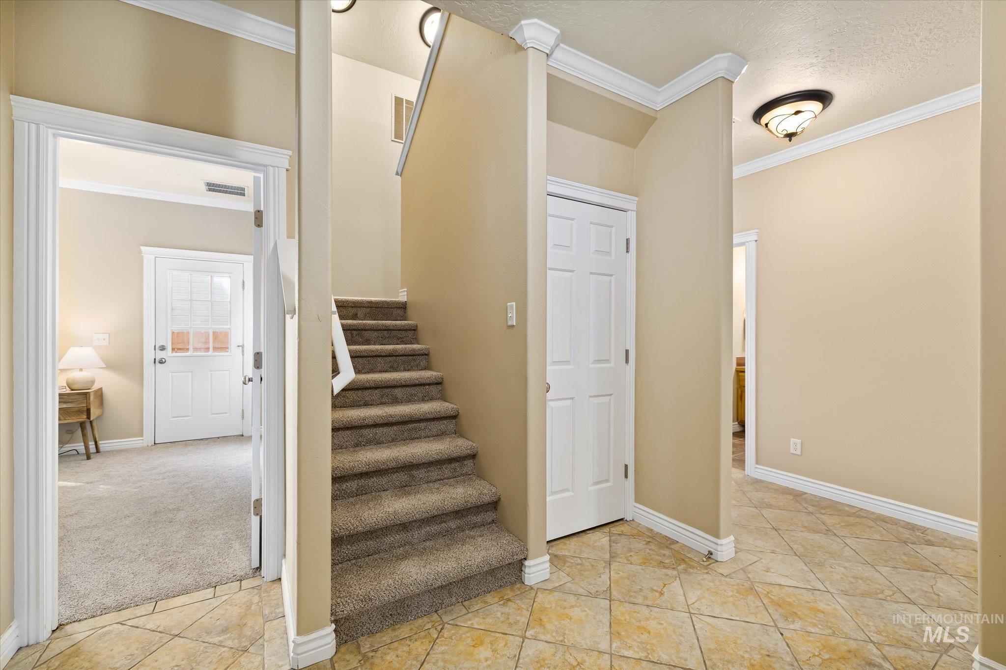 Stairway with crown molding, a textured ceiling, tile patterned floors, and carpet floors