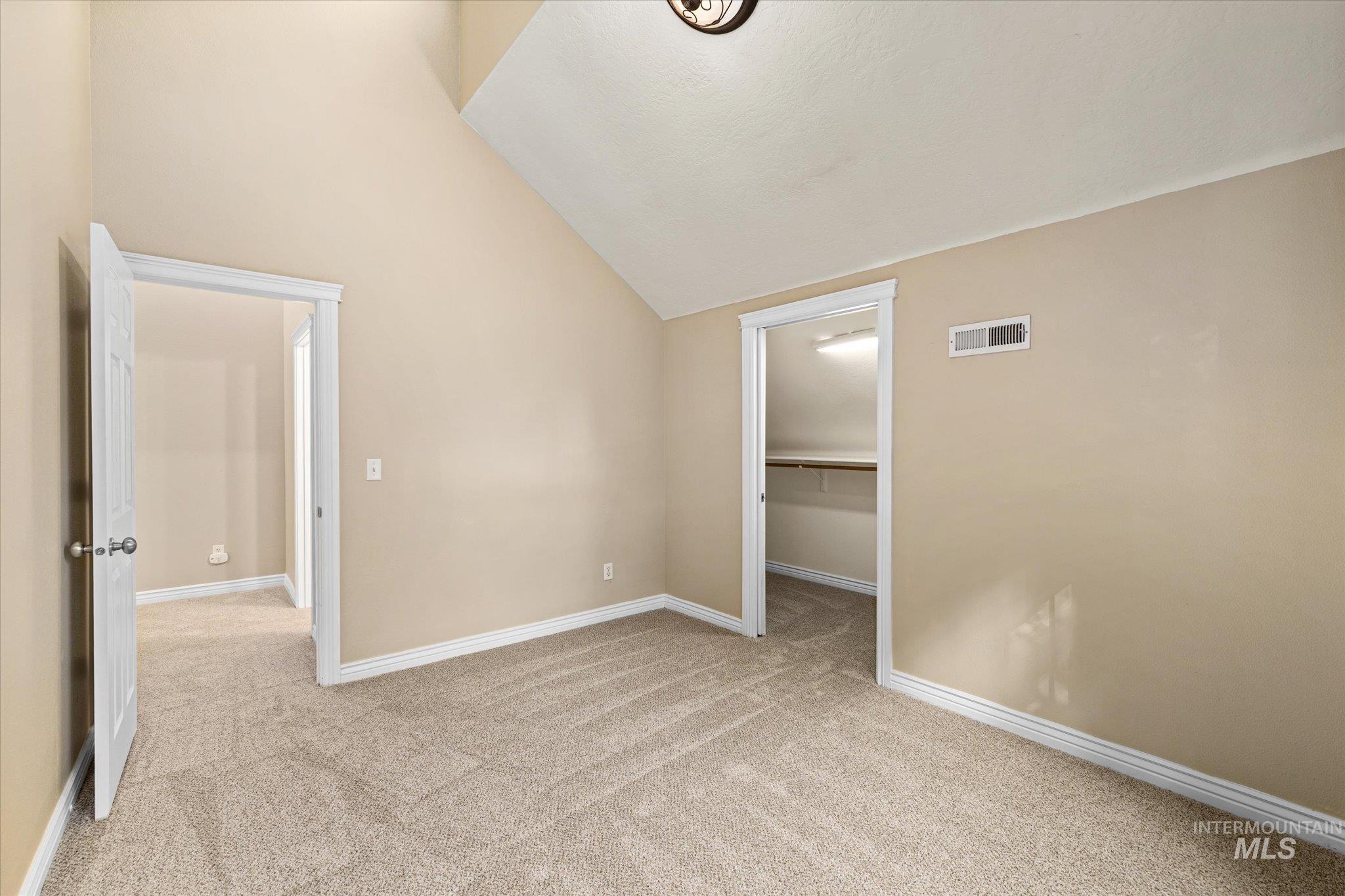 Unfurnished bedroom featuring a spacious closet, light colored carpet, lofted ceiling, and a textured ceiling