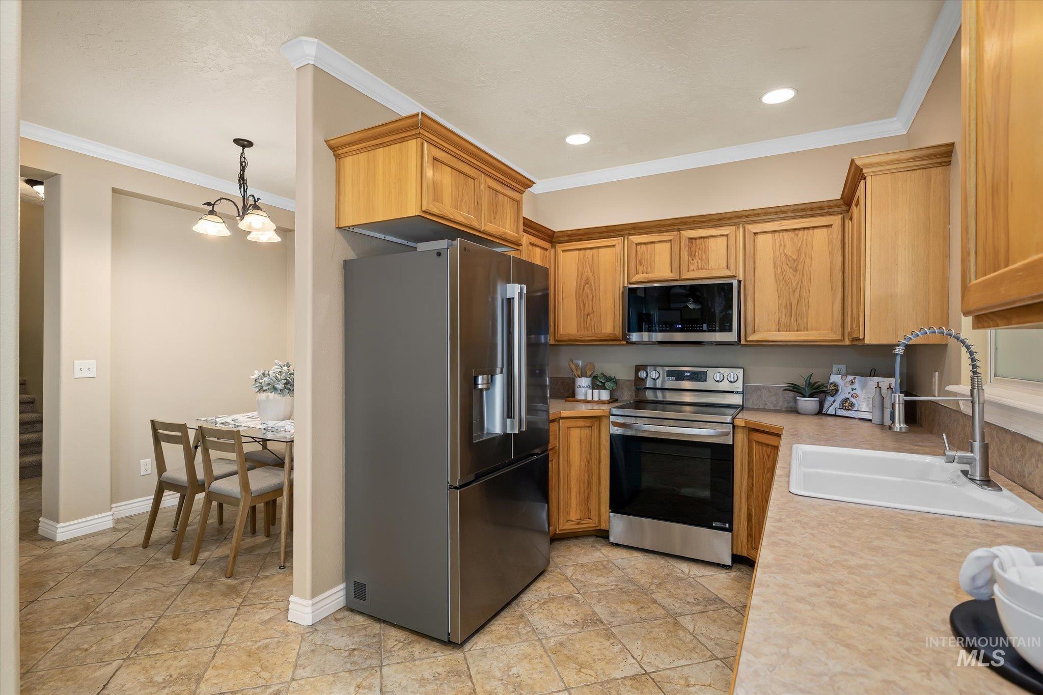 Kitchen featuring appliances with stainless steel finishes, light countertops, crown molding, hanging light fixtures, and a chandelier