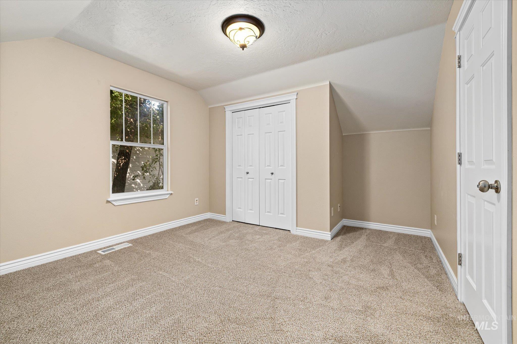 Unfurnished bedroom featuring lofted ceiling, light carpet, a closet, and a textured ceiling