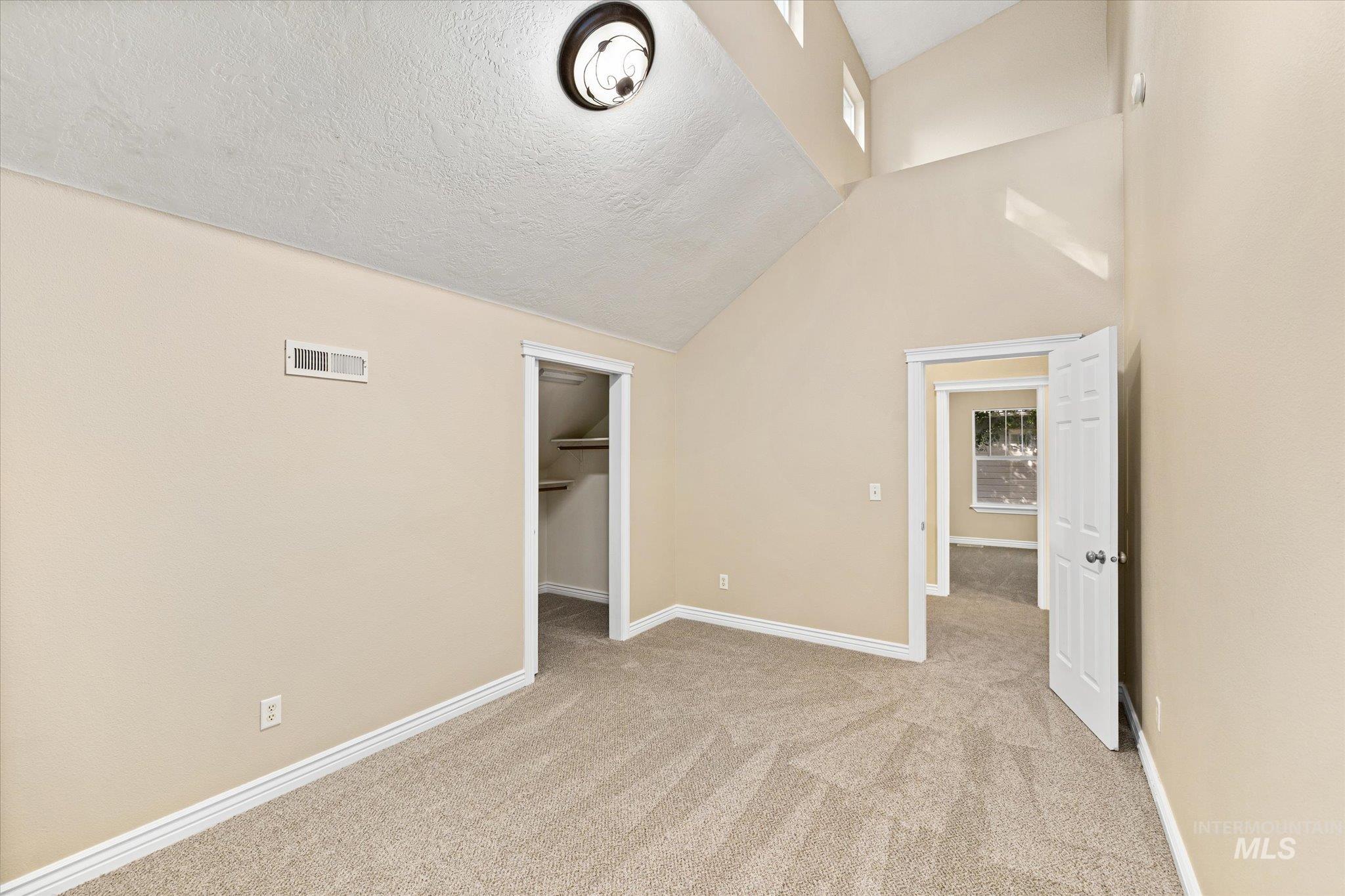 Unfurnished bedroom with light colored carpet, a spacious closet, a textured ceiling, and lofted ceiling