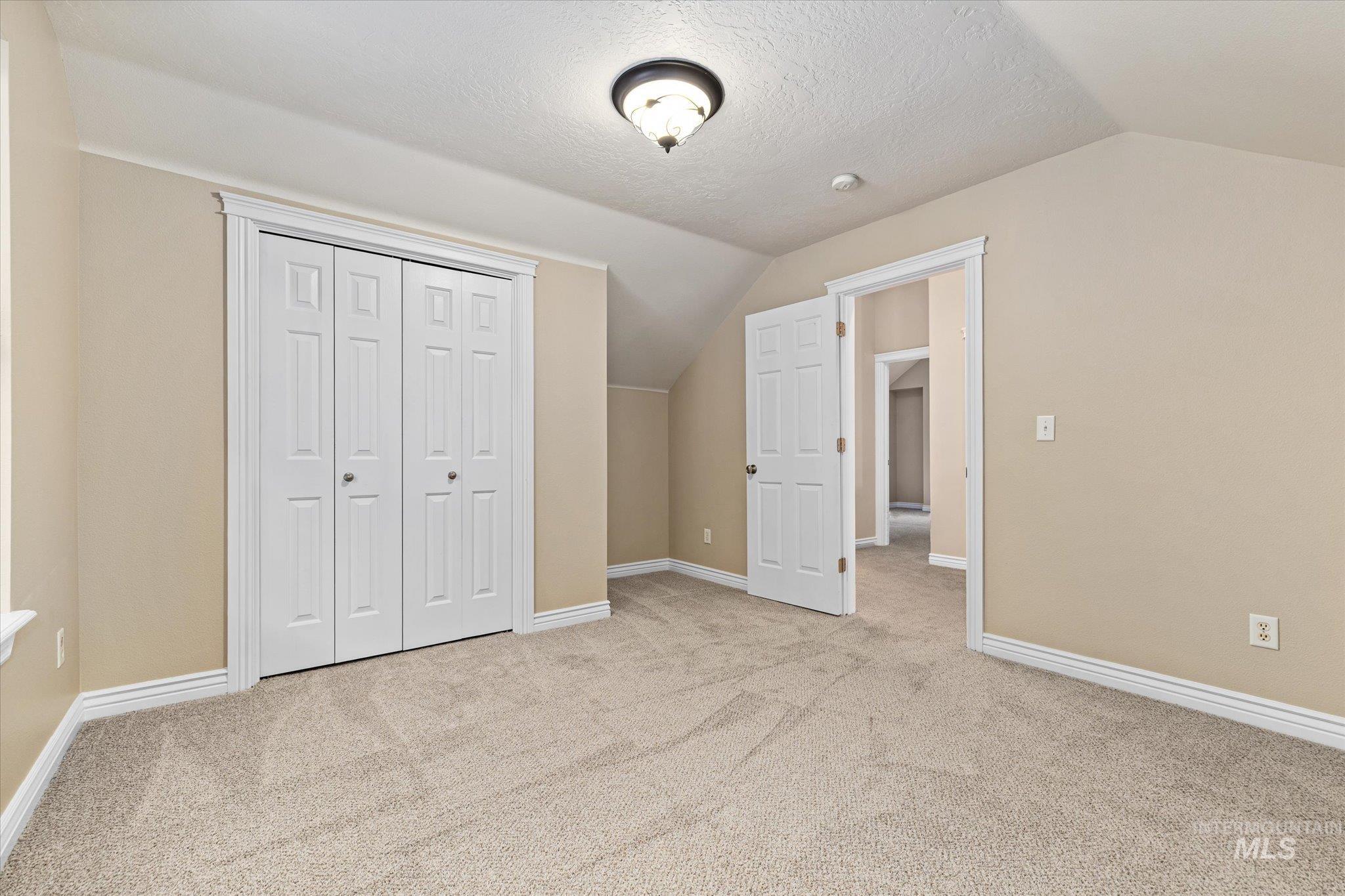 Unfurnished bedroom featuring lofted ceiling, a textured ceiling, light colored carpet, and a closet