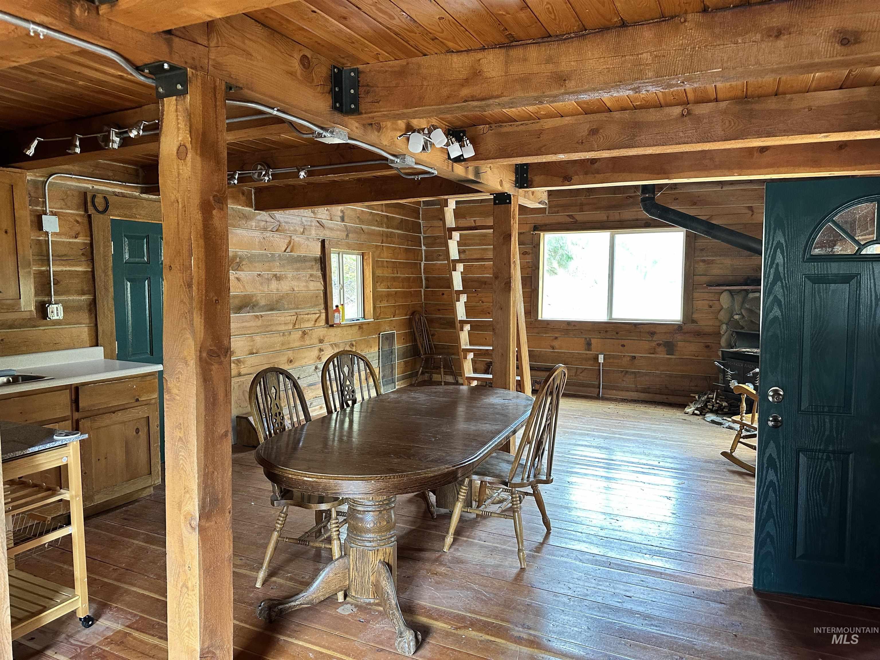 Dining area with plenty of natural light, dark wood finished floors, a wood ceiling with exposed beams, and wooden walls