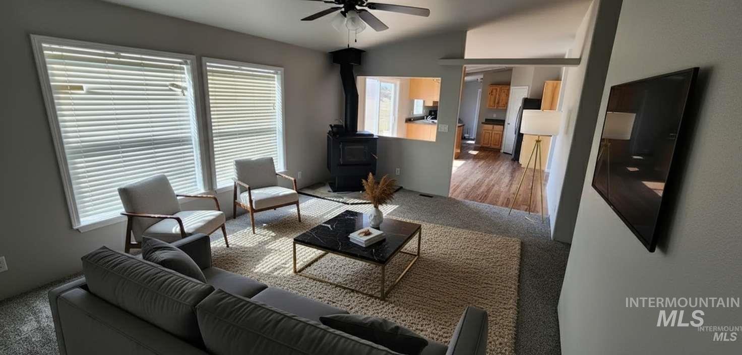 Carpeted living room with a wood stove, a ceiling fan, and vaulted ceiling
