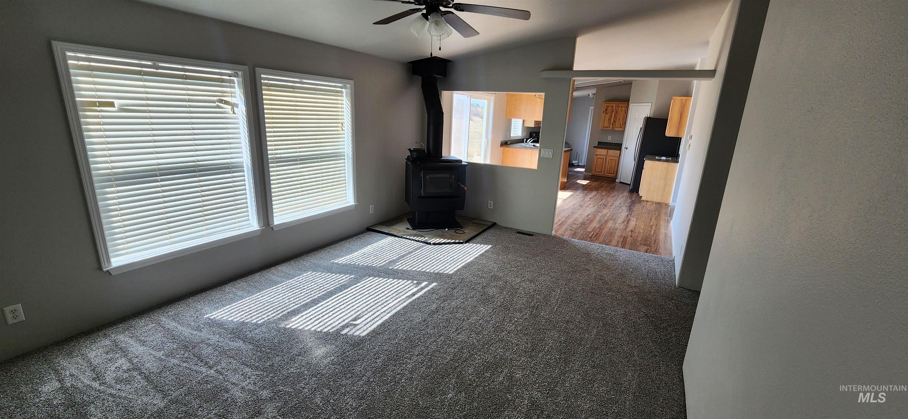 Unfurnished living room with a wood stove, dark carpet, ceiling fan, and lofted ceiling