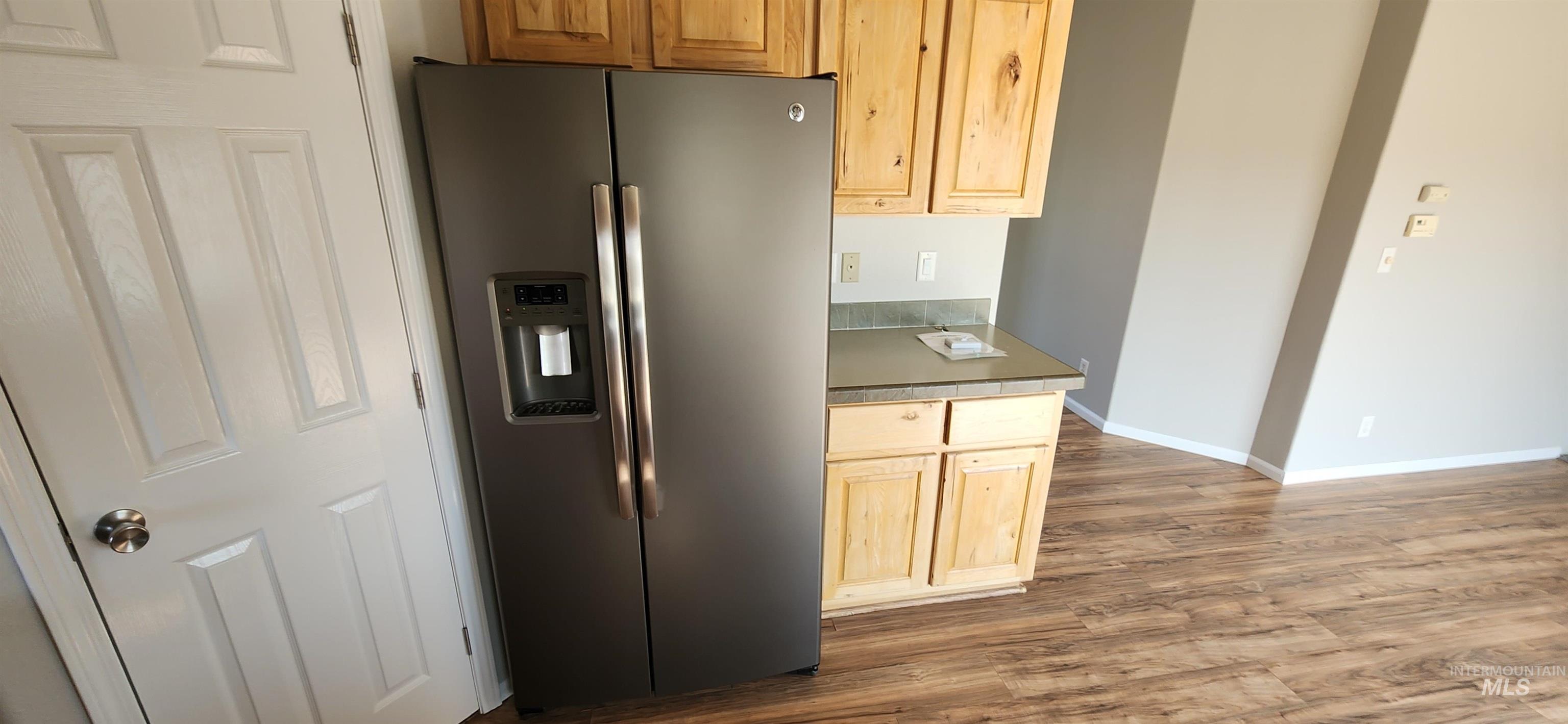 Kitchen featuring stainless steel refrigerator with ice dispenser, dark wood-style floors, light brown cabinetry, and dark countertops