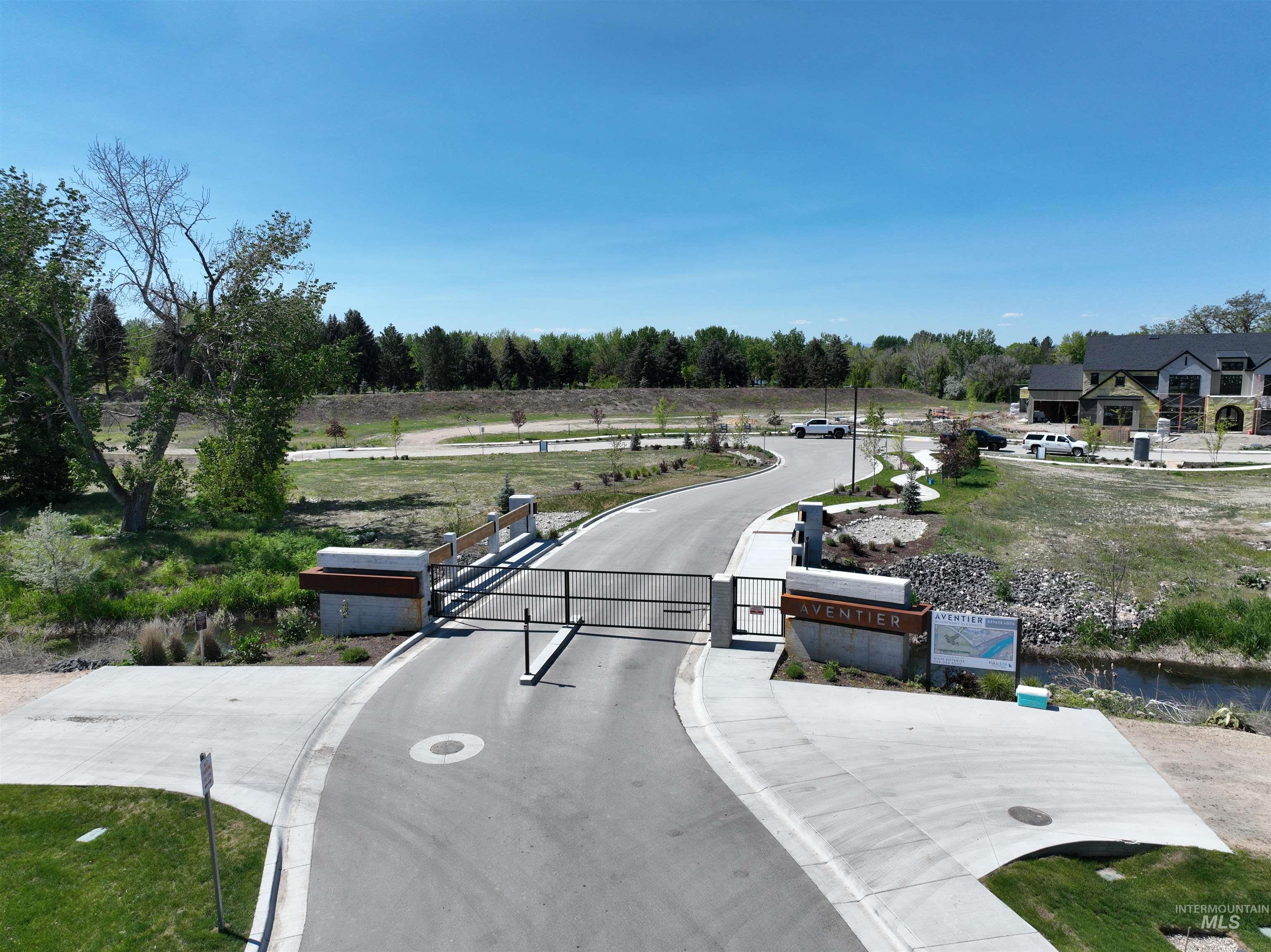 View of asphalt road featuring curbs, a gate, a gated entry, view of scattered trees, and sidewalks