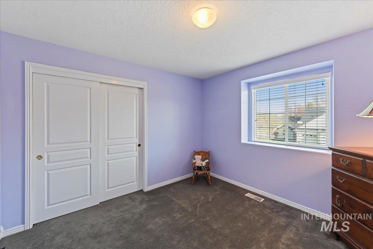 Unfurnished bedroom featuring dark carpet, a textured ceiling, and a closet