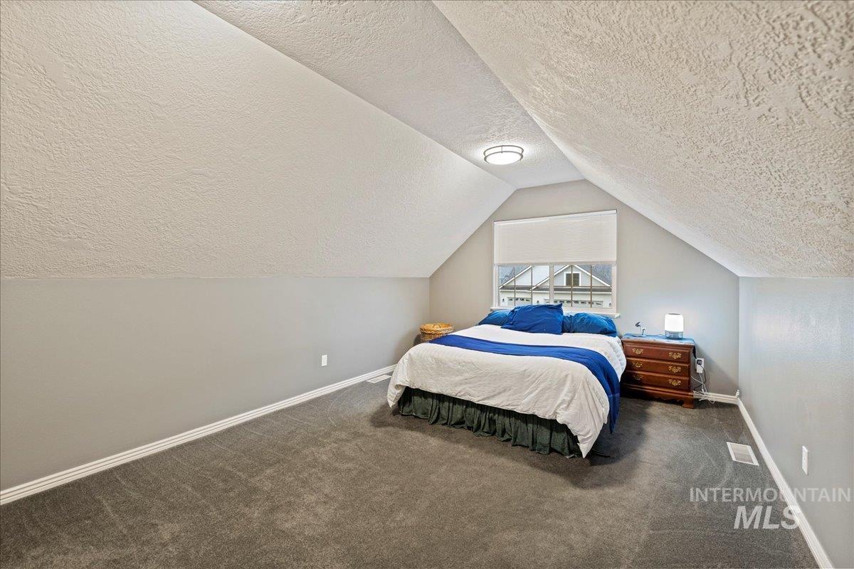 Bedroom featuring dark carpet, a textured ceiling, and vaulted ceiling