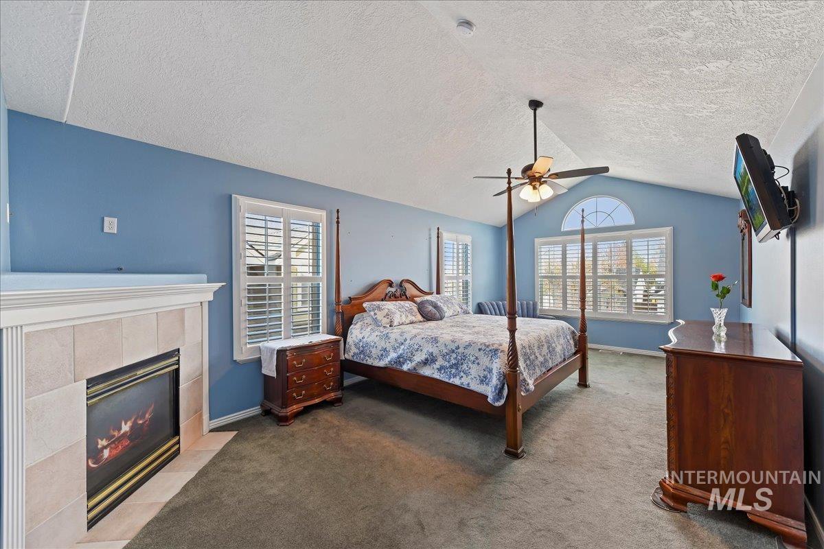 Bedroom featuring carpet, multiple windows, ceiling fan, vaulted ceiling, and a tiled fireplace