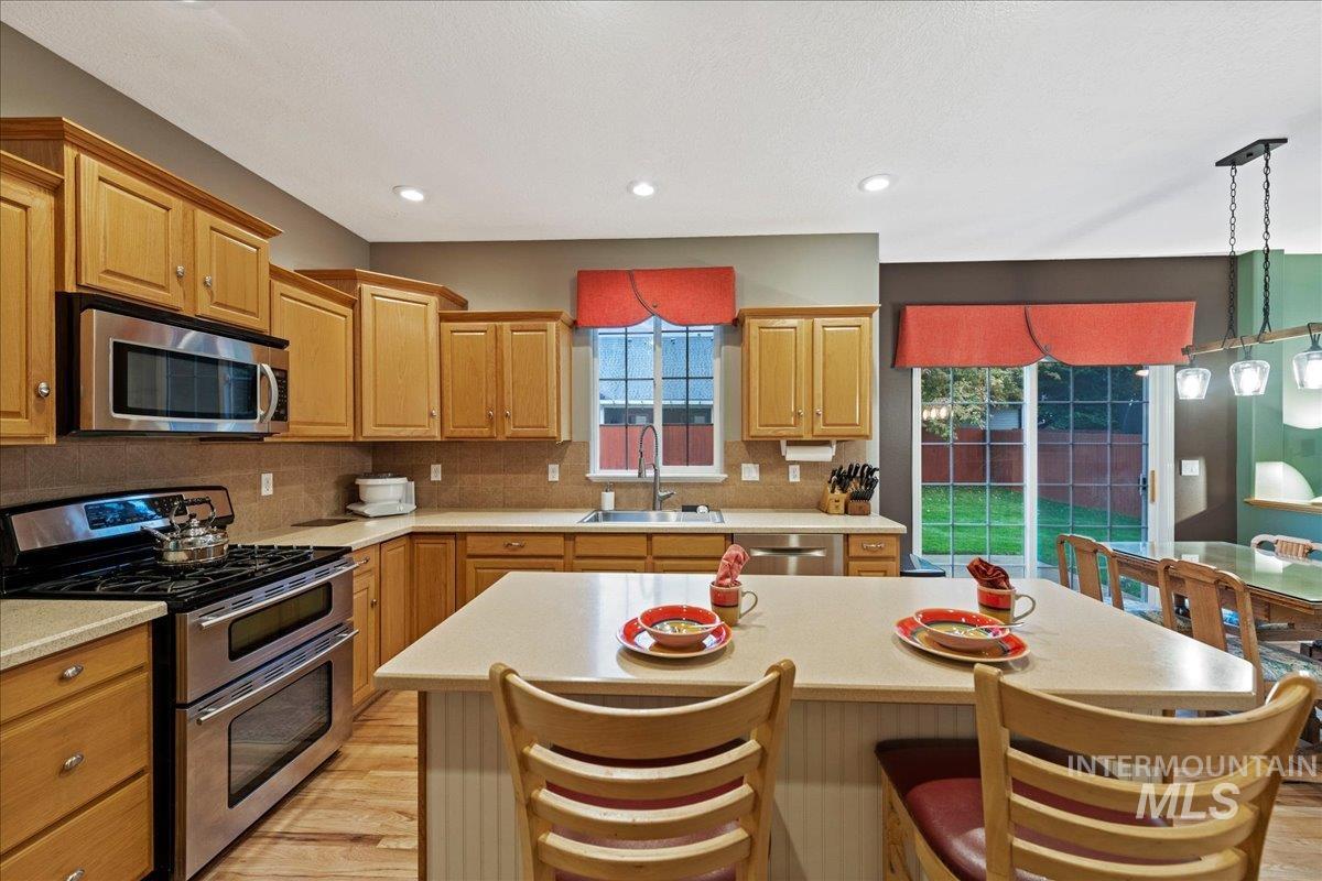 Kitchen with appliances with stainless steel finishes, pendant lighting, light wood-style floors, a center island, and decorative backsplash