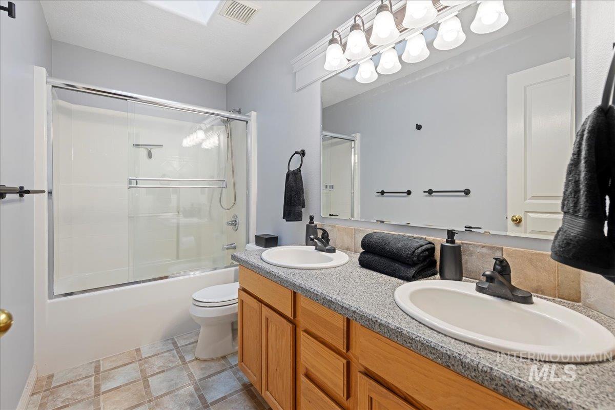 Full bathroom featuring double vanity and shower / bath combination with glass door