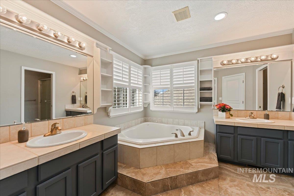 Full bath with two vanities, crown molding, a bath, a textured ceiling, and light tile patterned floors