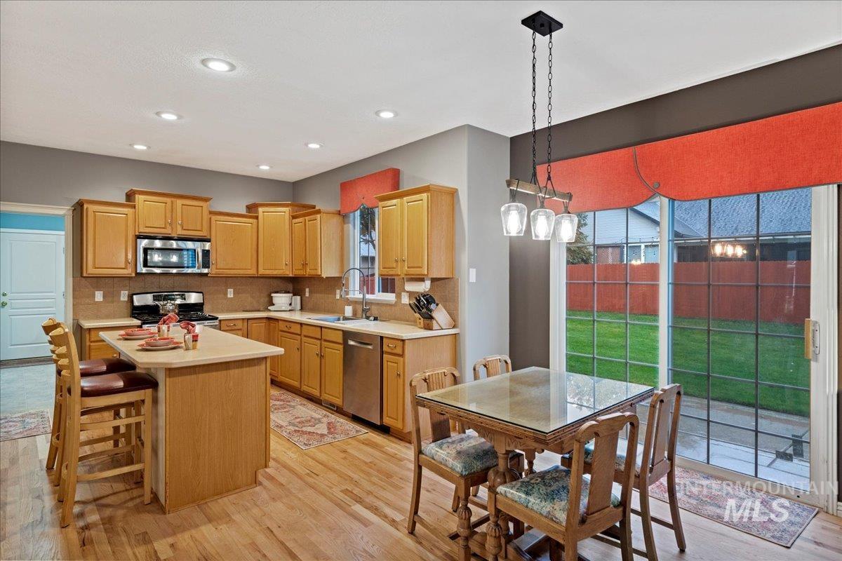 Kitchen with light wood-style floors, stainless steel appliances, hanging light fixtures, decorative backsplash, and recessed lighting