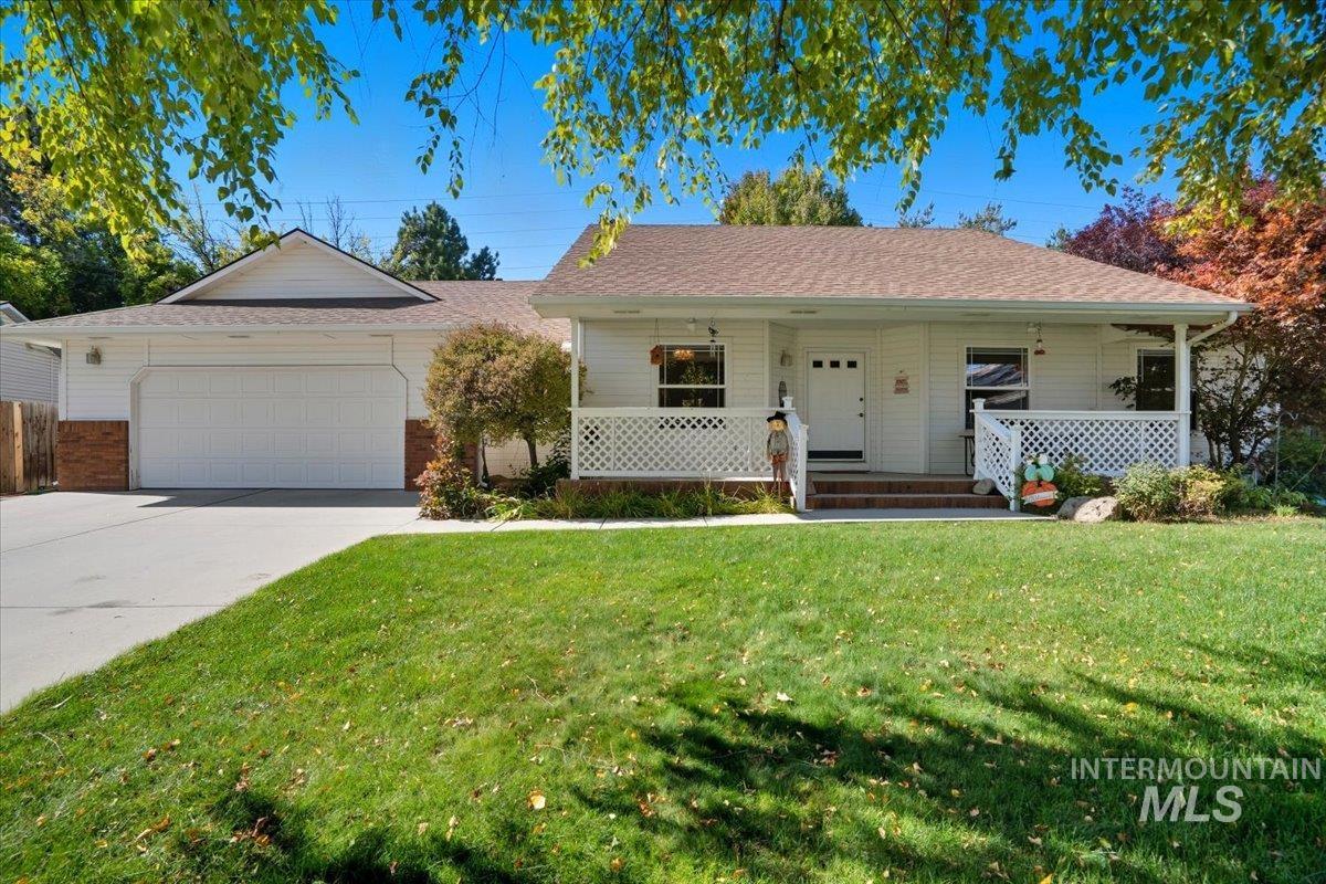 Front of home featuring covered porch, a front lawn, driveway, an attached garage, and mature landscaping