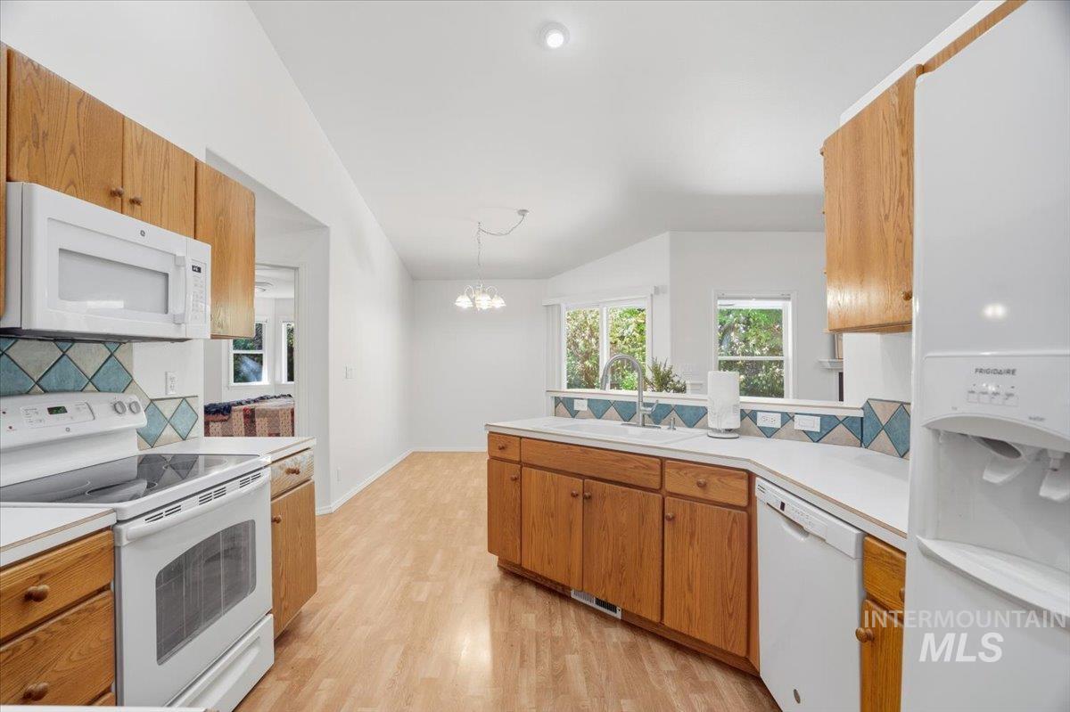 Kitchen featuring decorative backsplash, white appliances, wood cabinetry, light laminate floors, and light countertops