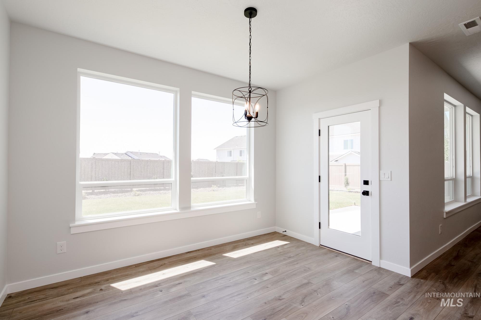 Unfurnished dining area with a chandelier, wood finished floors, and healthy amount of natural light